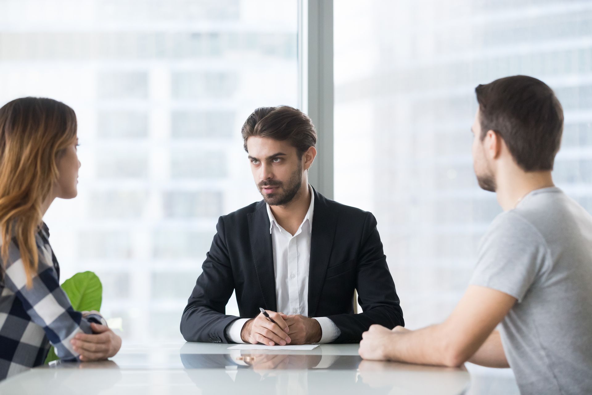 Man in suit at table with two people; discussing, serious expressions, office.