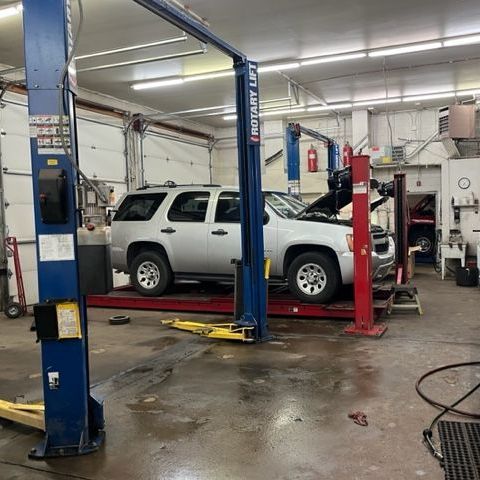 A silver suv is on a lift in a garage.