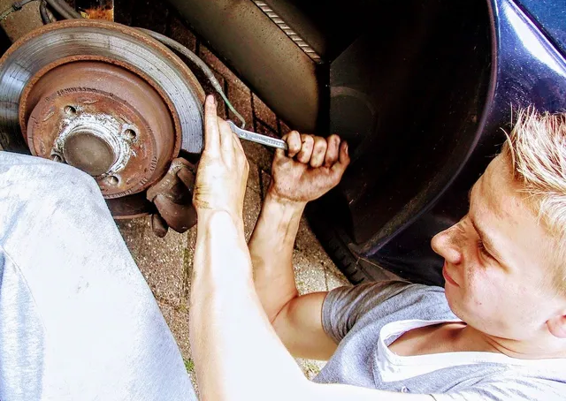 Person working on a car brake, using a wrench. Mechanic in a garage.