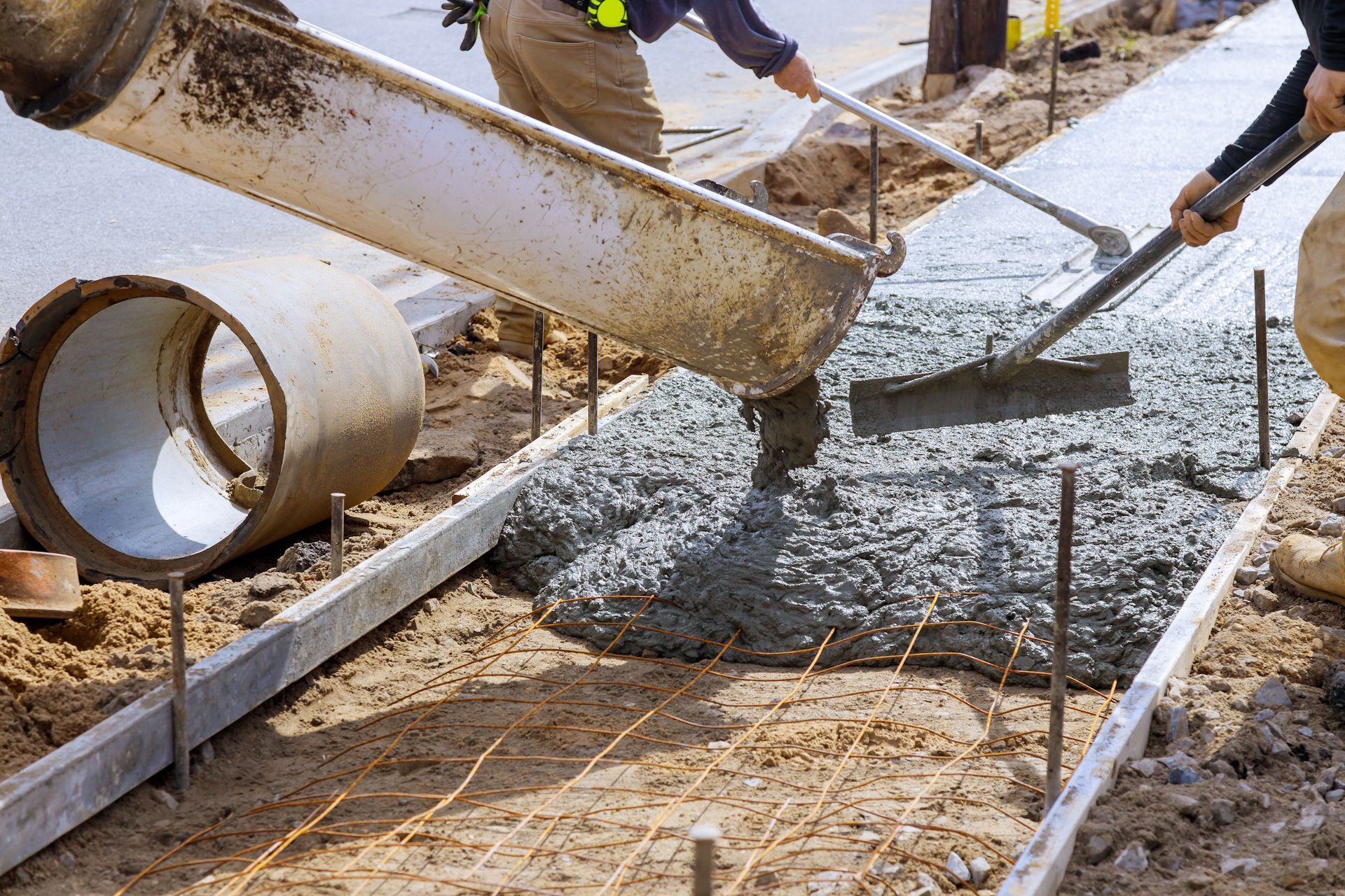 A man is pouring concrete on a sidewalk with a rake.