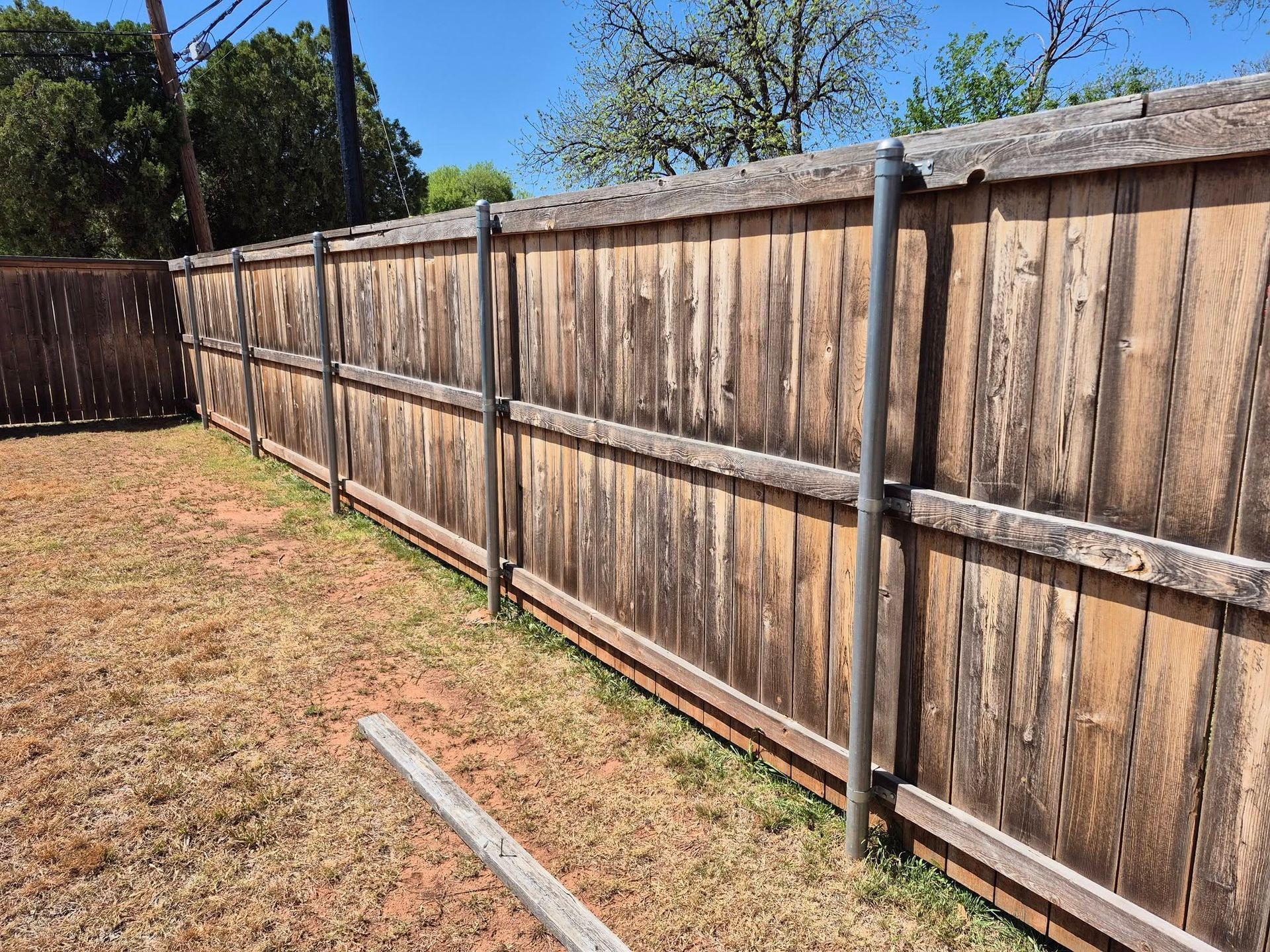 Wooden backyard fence along a dry grass yard under a clear blue sky