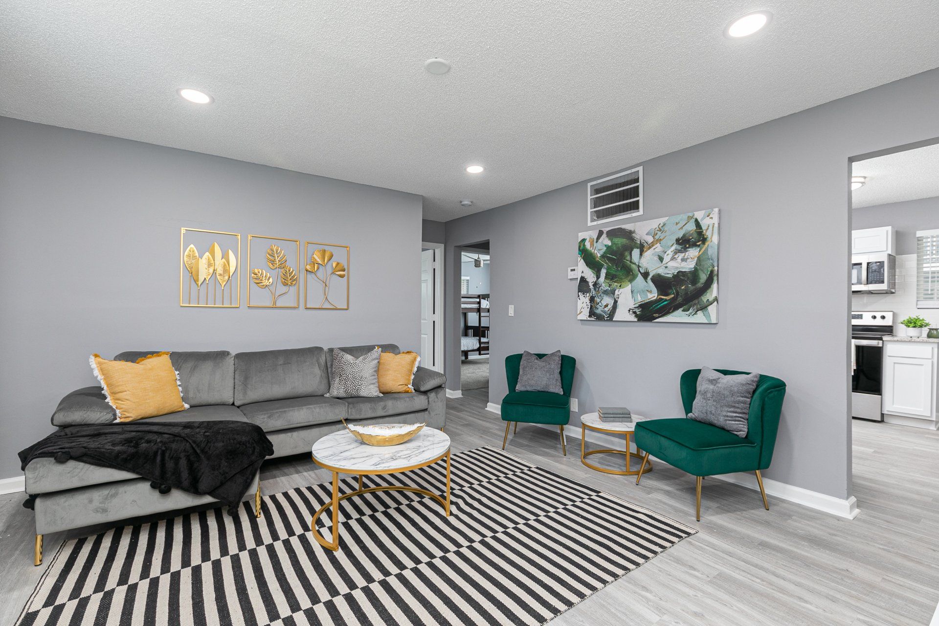 Apartments Near Tyler Perry Studios in Sylvan Hills, GA - Gateway South Apartments - Virtually Staged Living Room with Grey Walls, Faux Wood Flooring, Wall Art, and Green Chairs