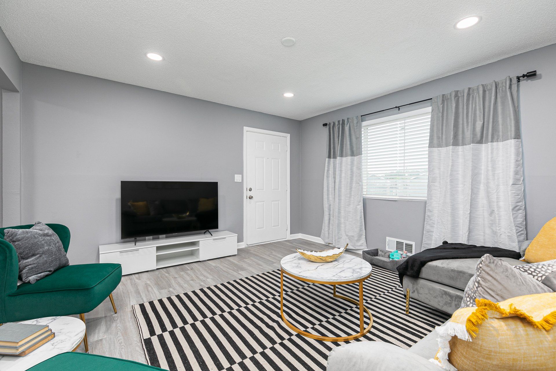 Two-Bedroom Apartments In Sylvan Hills, GA - Gateway South - Cozy Living Room With Faux Wood Flooring, Area Rug, Sectional Couch, Wingback Chair, Round Coffee Table, Media Cabinet, TV, And Window.