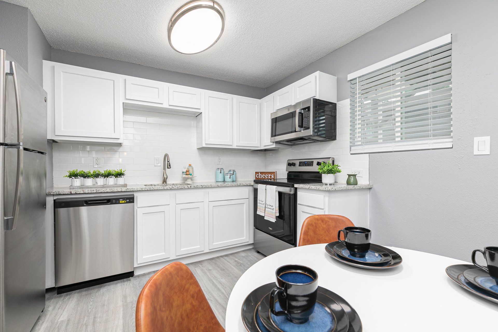 Atlanta, GA Apartments - Gateway South - Kitchen With Faux Wood Flooring, Electric Stainless Steel Appliances, Built-In Microwave, White Cabinets, And Dining Table.