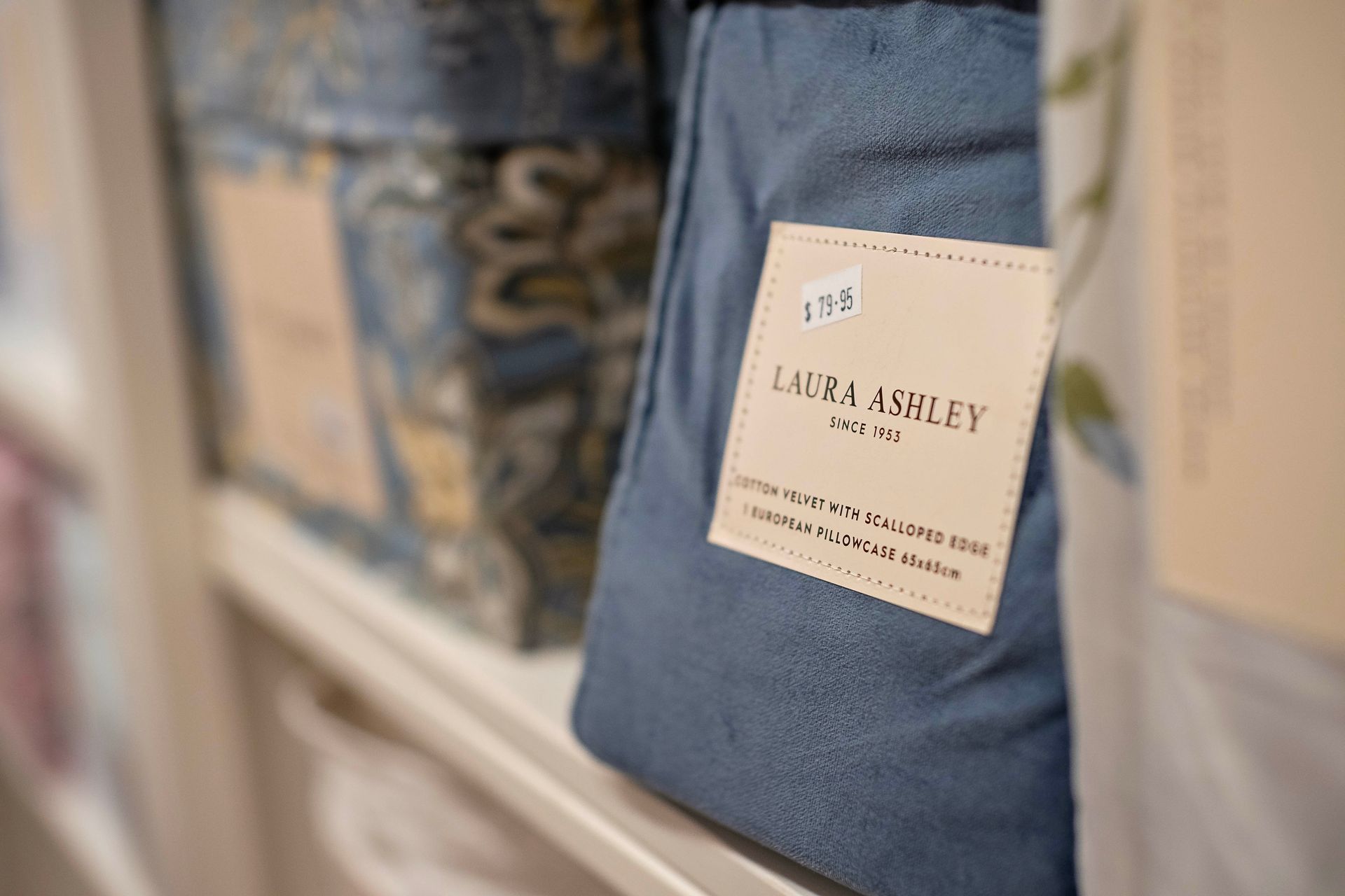 Blue Laura Ashley pillow with price tag on a shelf.