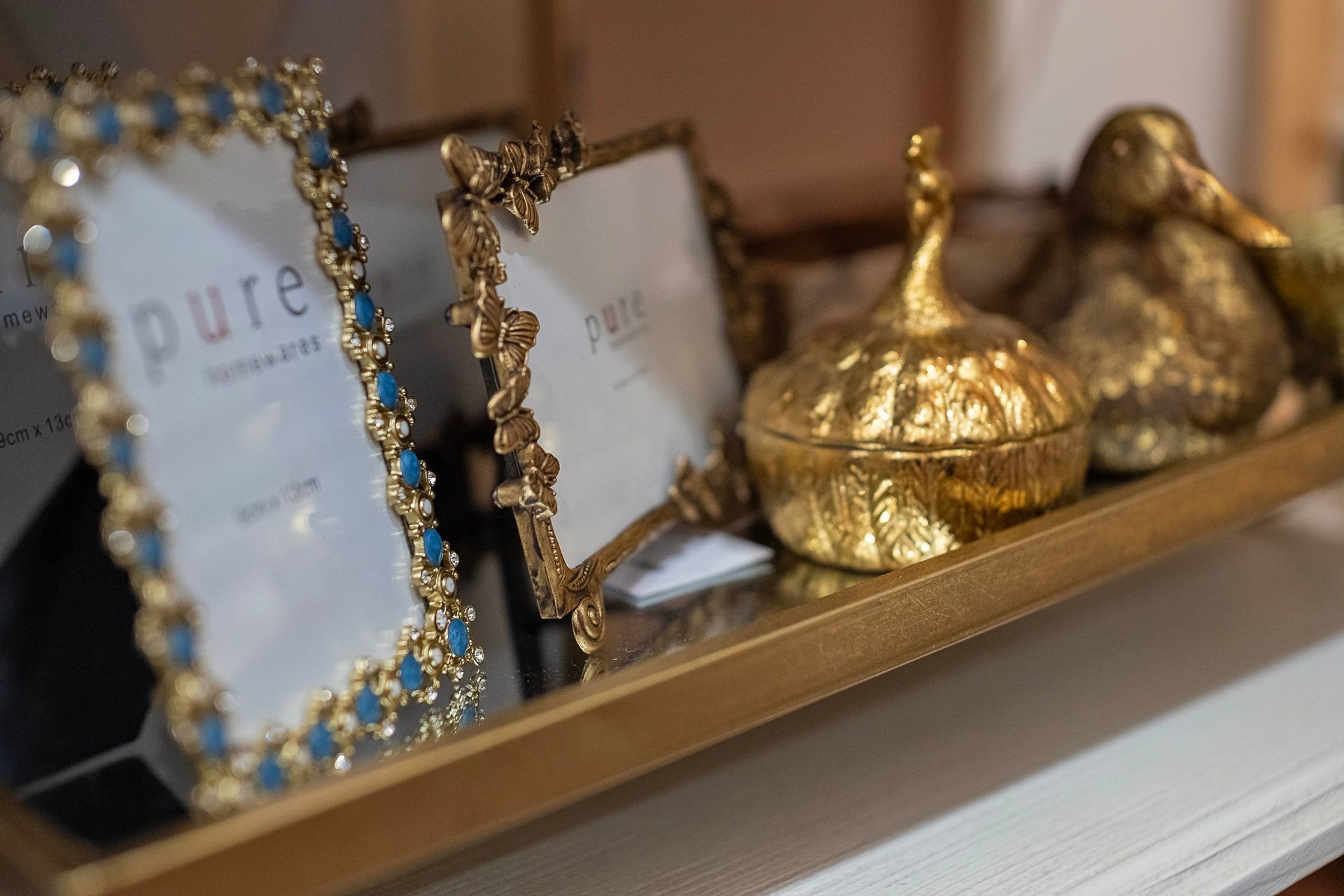 Gold tray with decorative items: picture frames, a lidded jar, and a figurine.