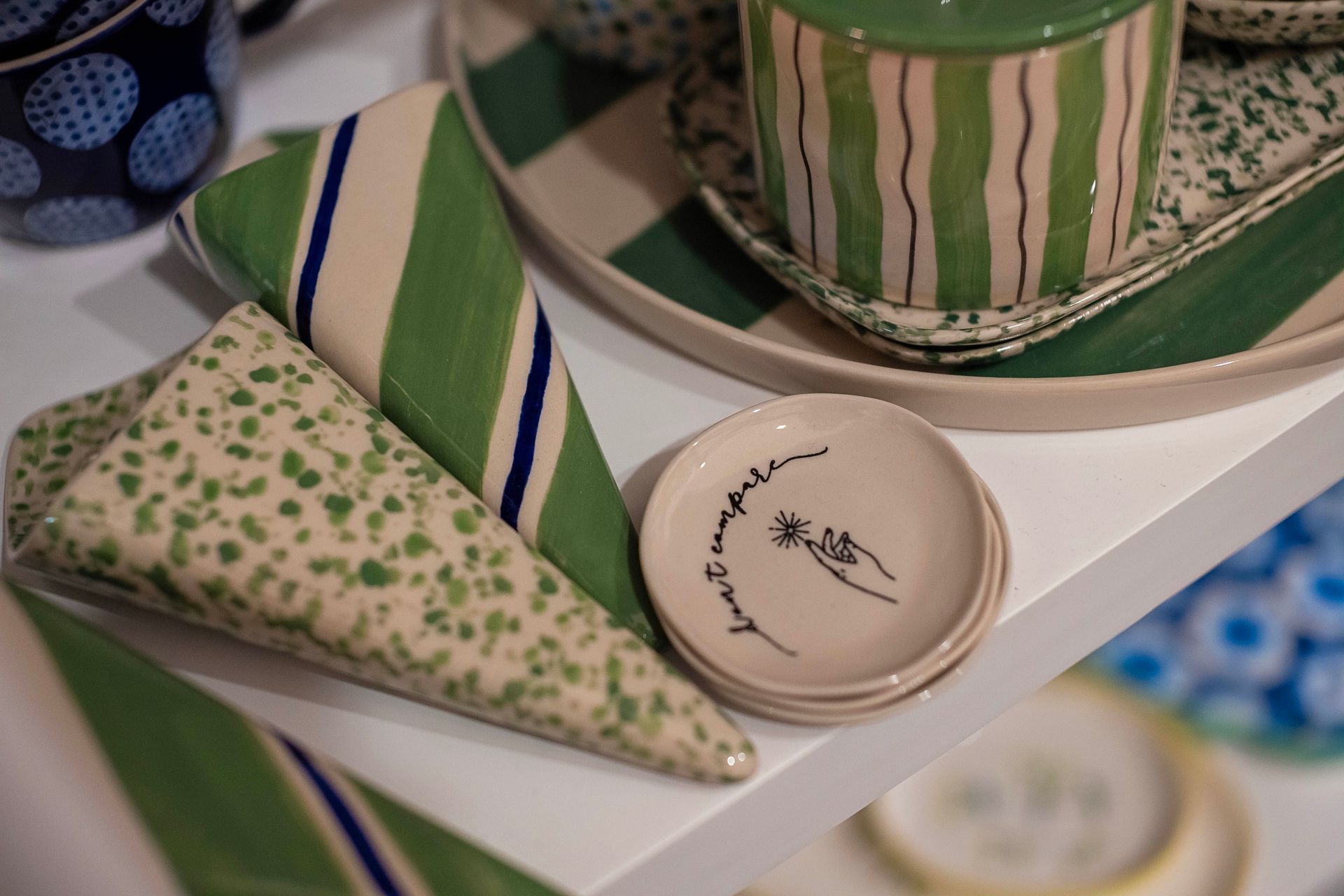 Ceramic tableware with green and white striped, dotted, and floral patterns on a shelf.