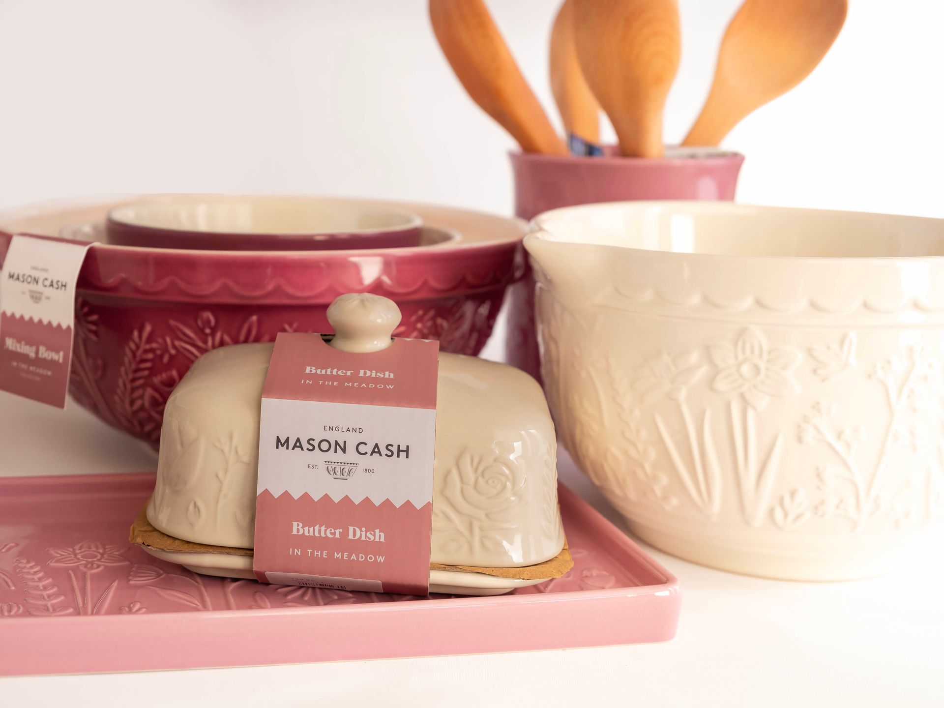 Cream-coloured kitchenware set, including bowls and a butter dish, on a white surface with pink accents.