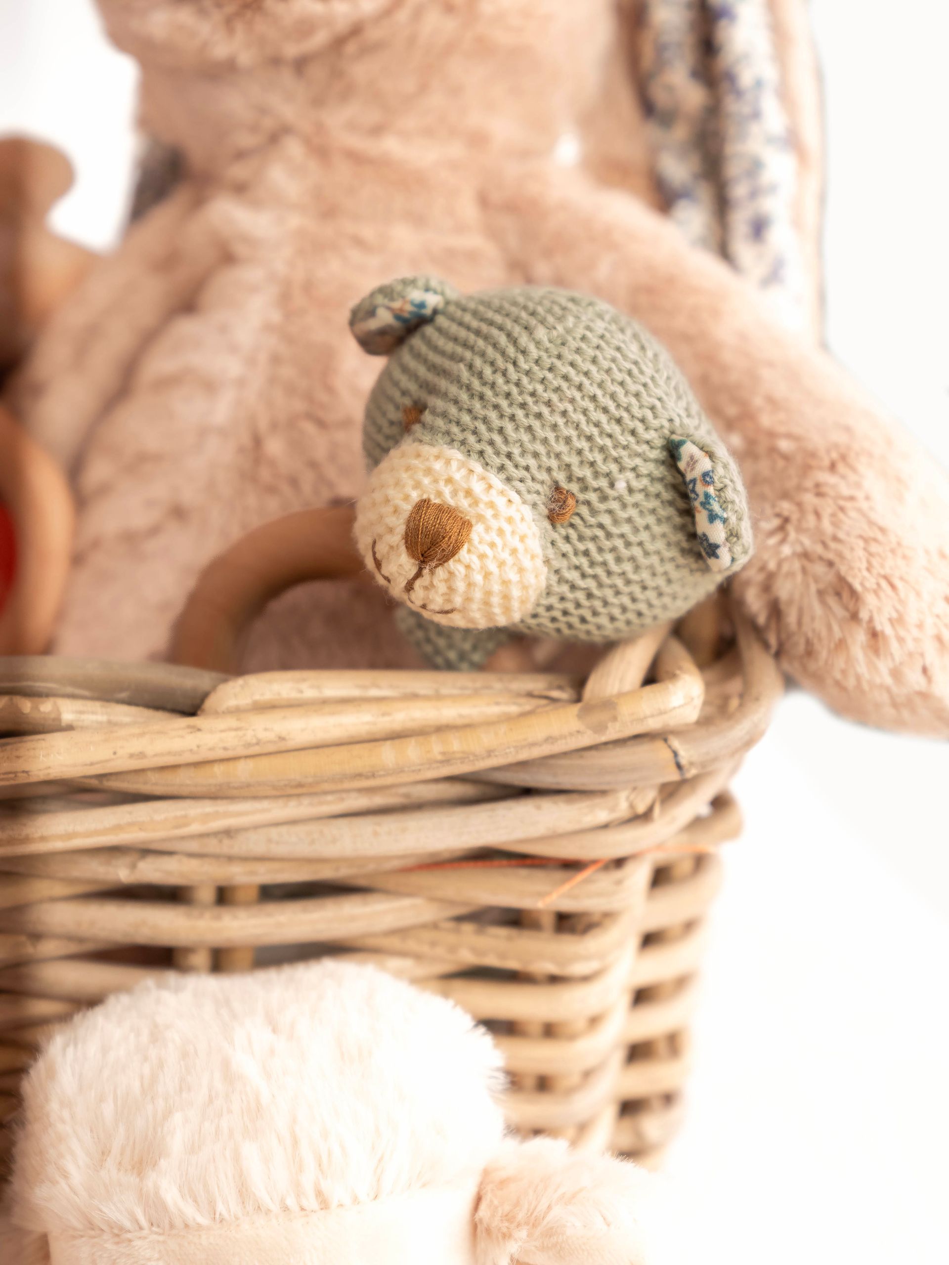 Close-up of a knit teddy bear in a wicker basket with a larger bunny plush behind it.