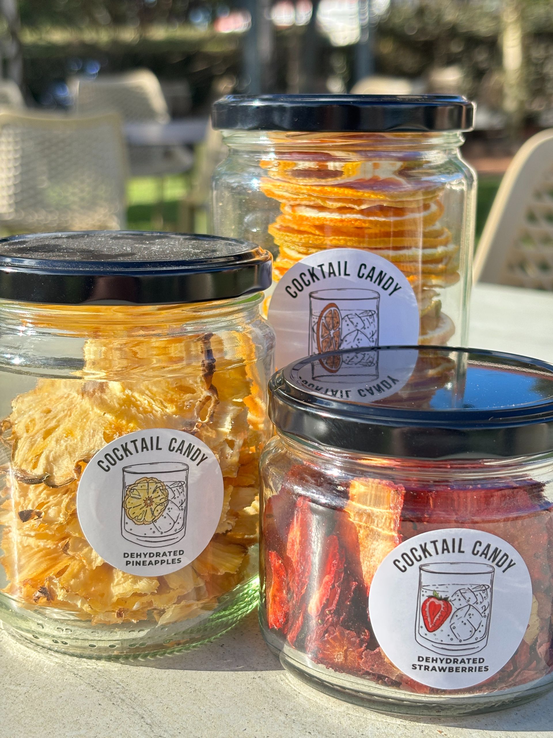 Three glass jars of cocktail candy with black lids, outdoors.