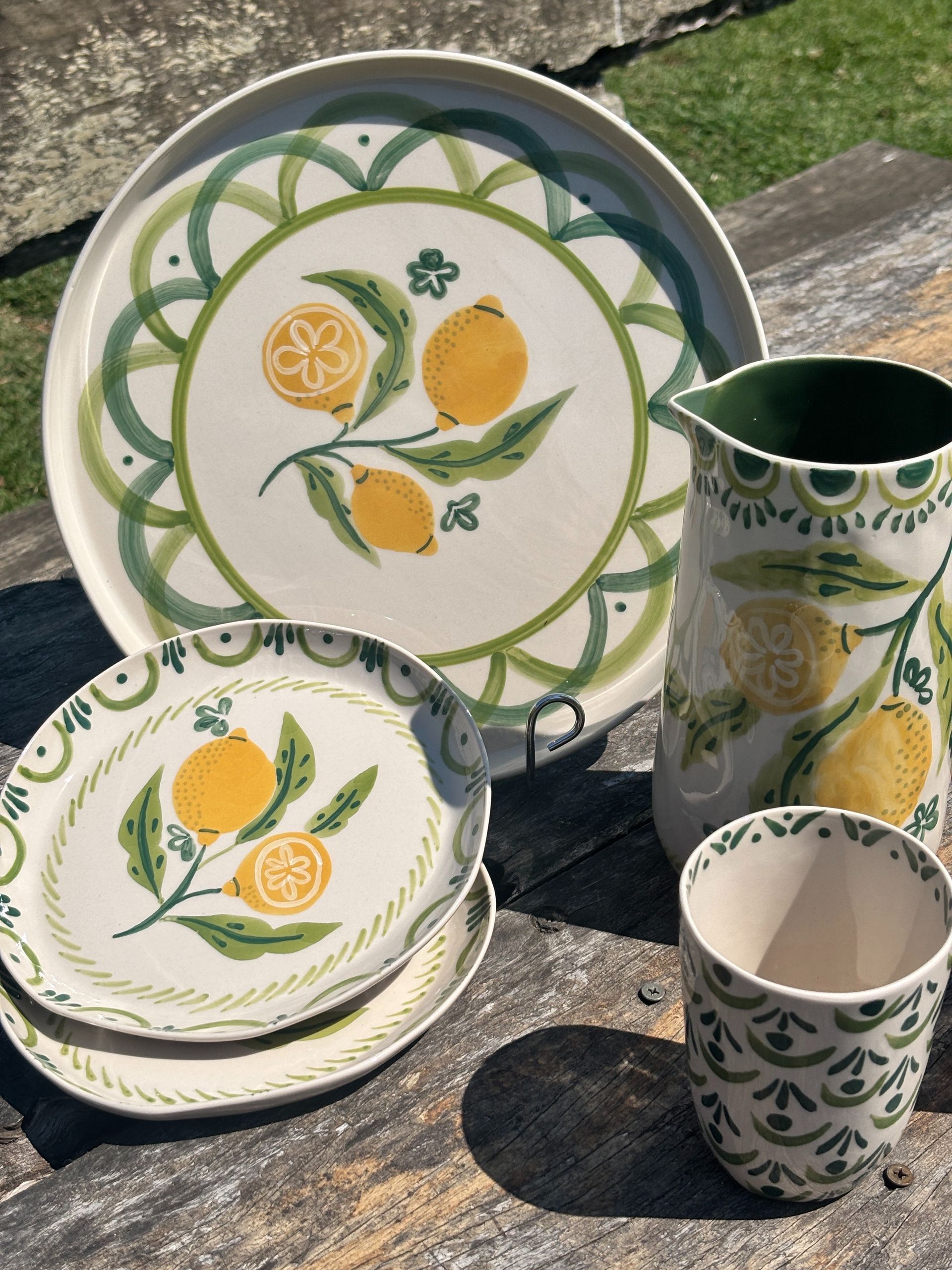 Lemon-themed ceramic tableware set: plate, plates, pitcher, and cup. Yellow lemons with green leaves on white.