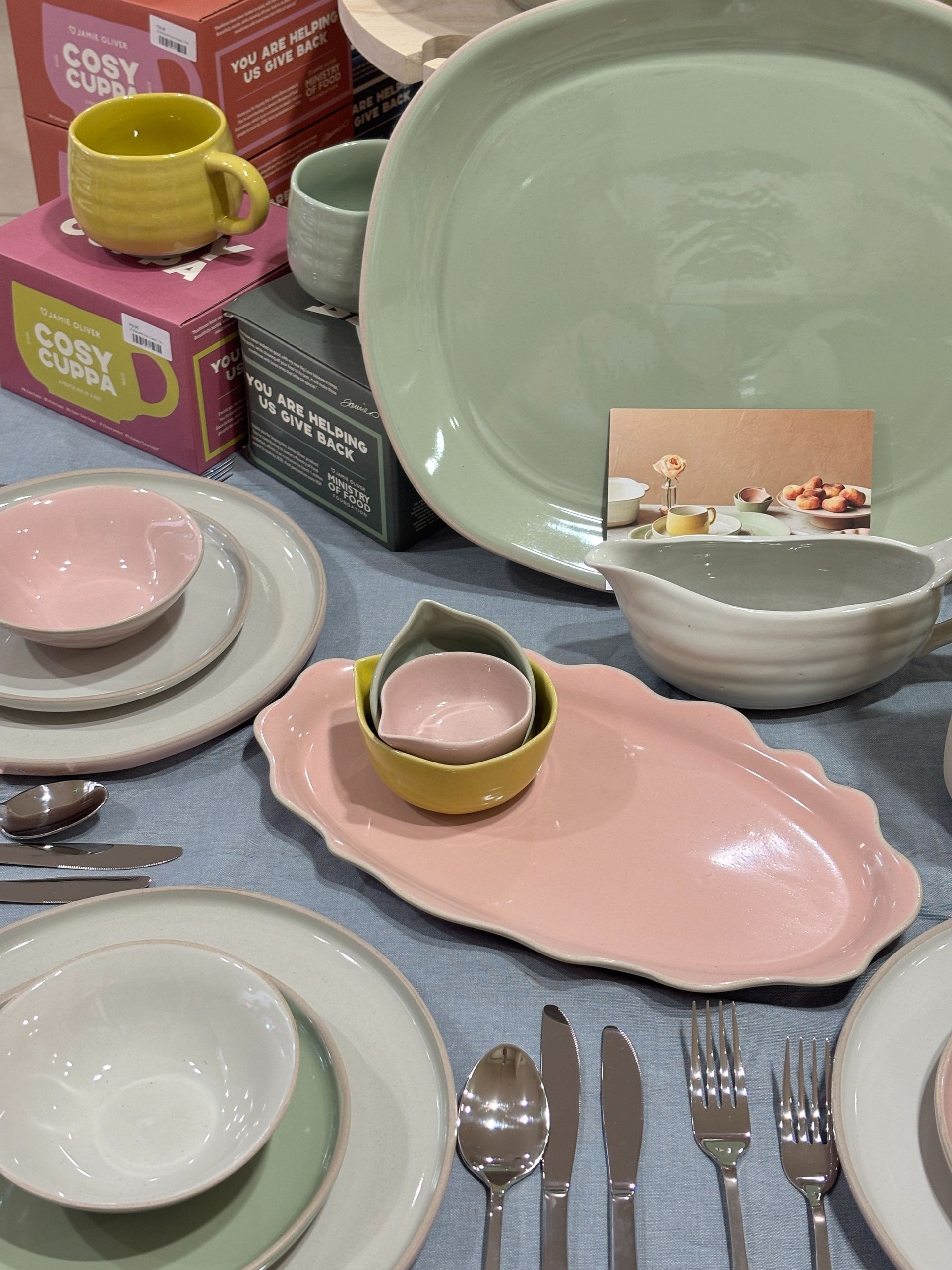 Ceramic dish-ware in pastel colours, including plates, bowls, cups, and serving dishes arranged on a light blue tablecloth.