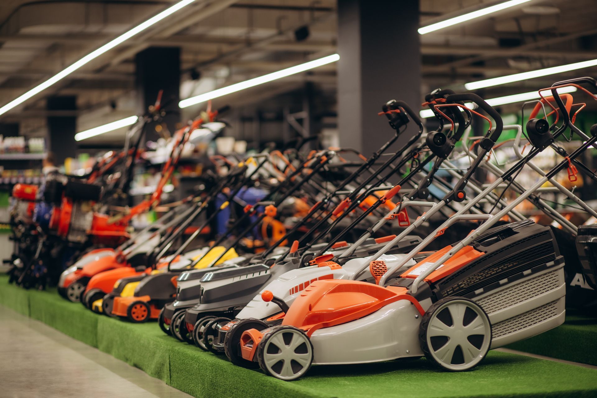 Lawn mowers displayed for sale in a store. Several with orange and white colors, arranged on green display.