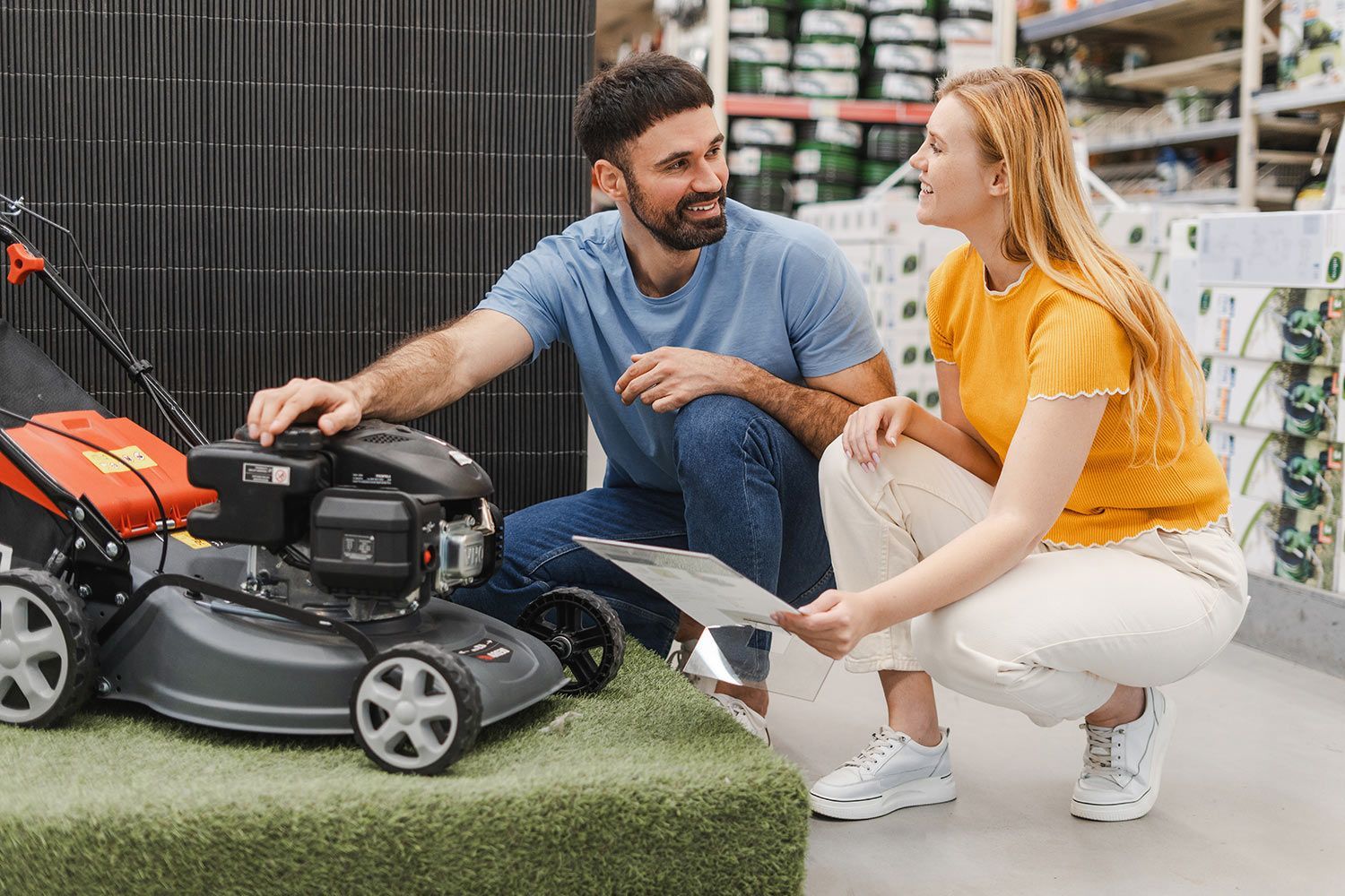 Two people examine a lawn mower together inside a home improvement store.