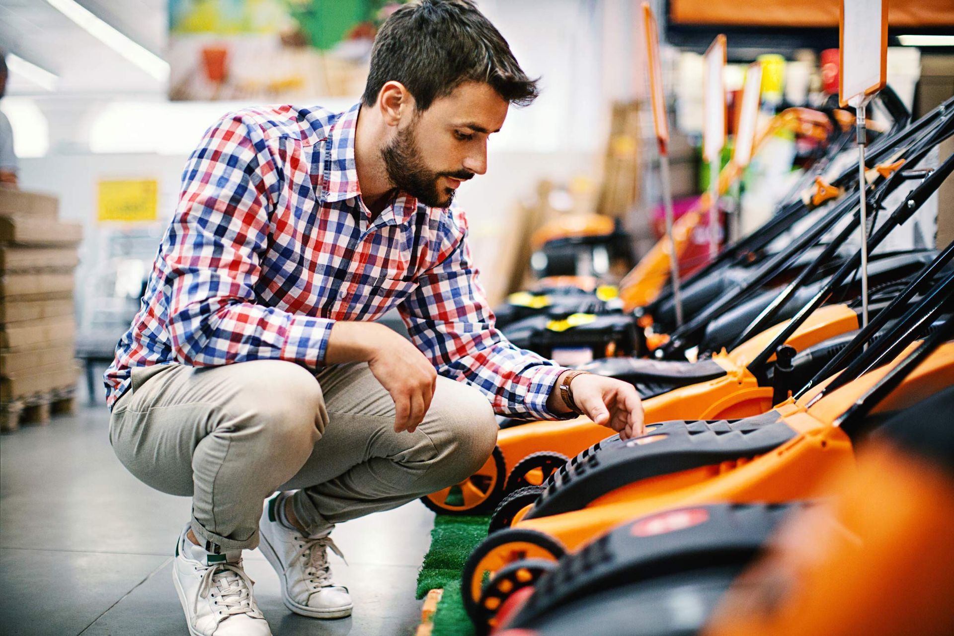 A young man is choosing an orange lawn mower at a local lawn mower store.
