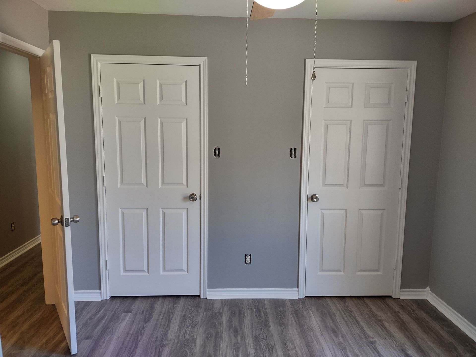 A bedroom with two white doors and a wooden floor.
