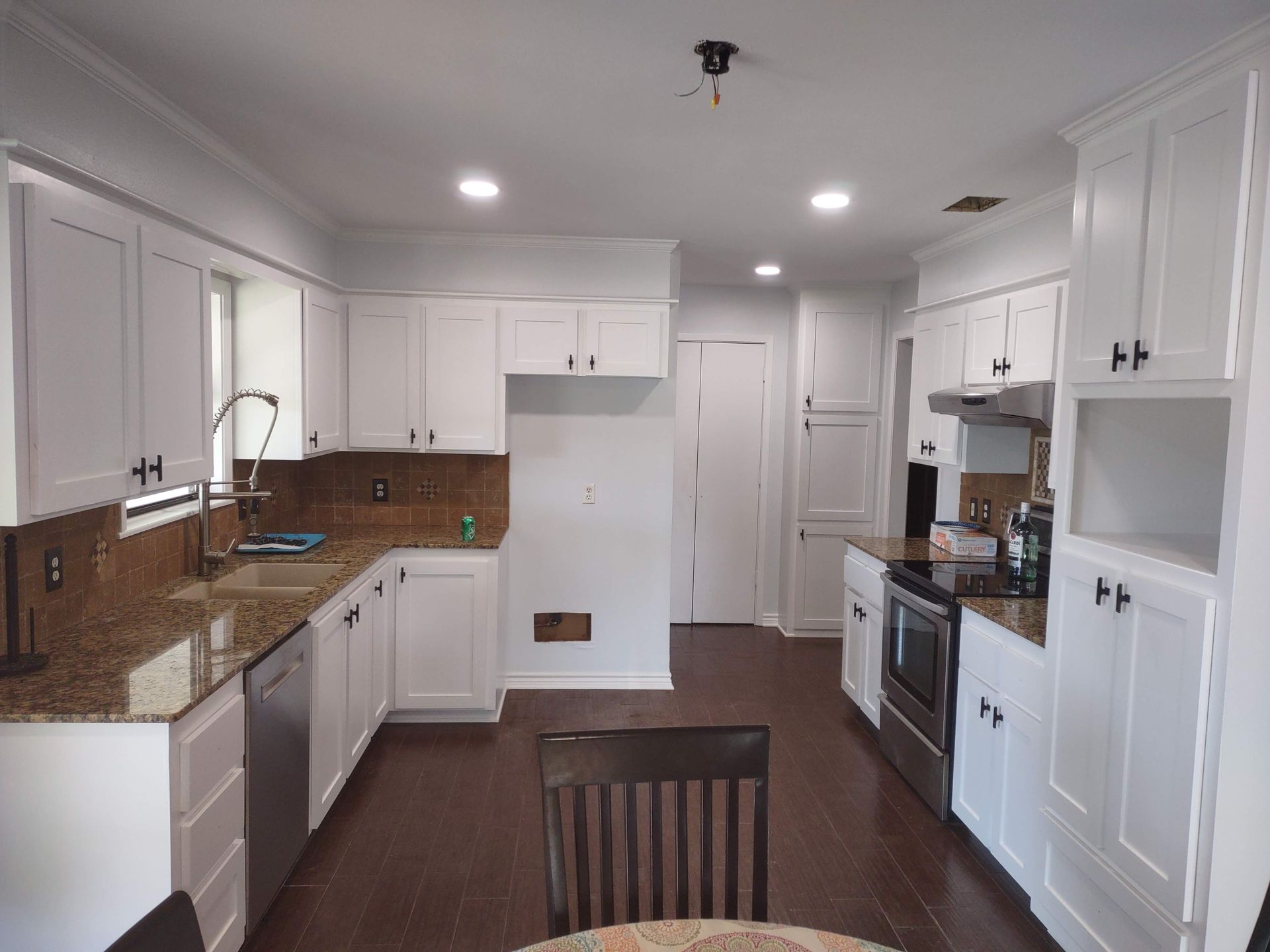 A kitchen with white cabinets , granite counter tops , stainless steel appliances and a table.