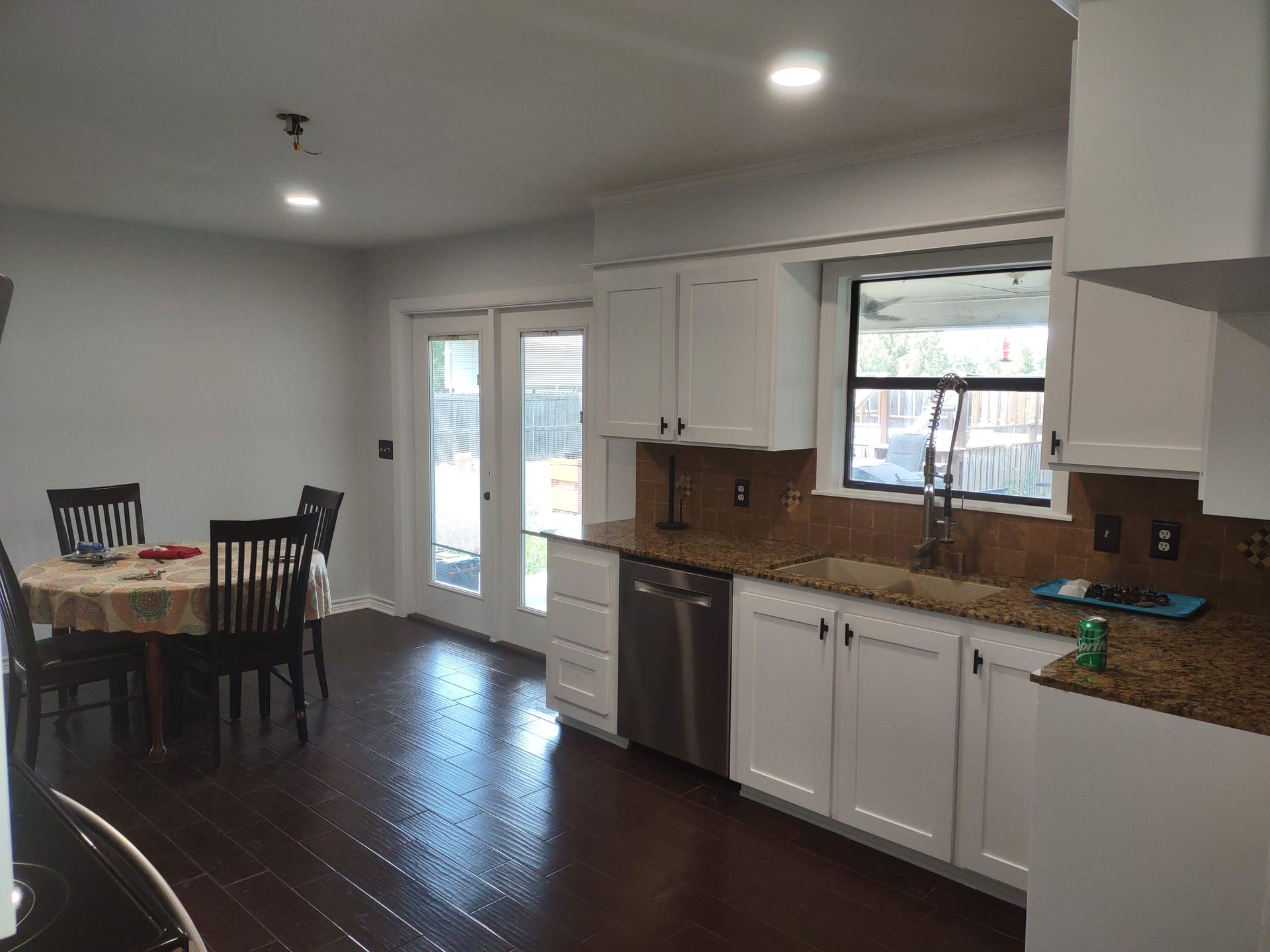 A kitchen with white cabinets , granite counter tops , stainless steel appliances and a table and chairs.