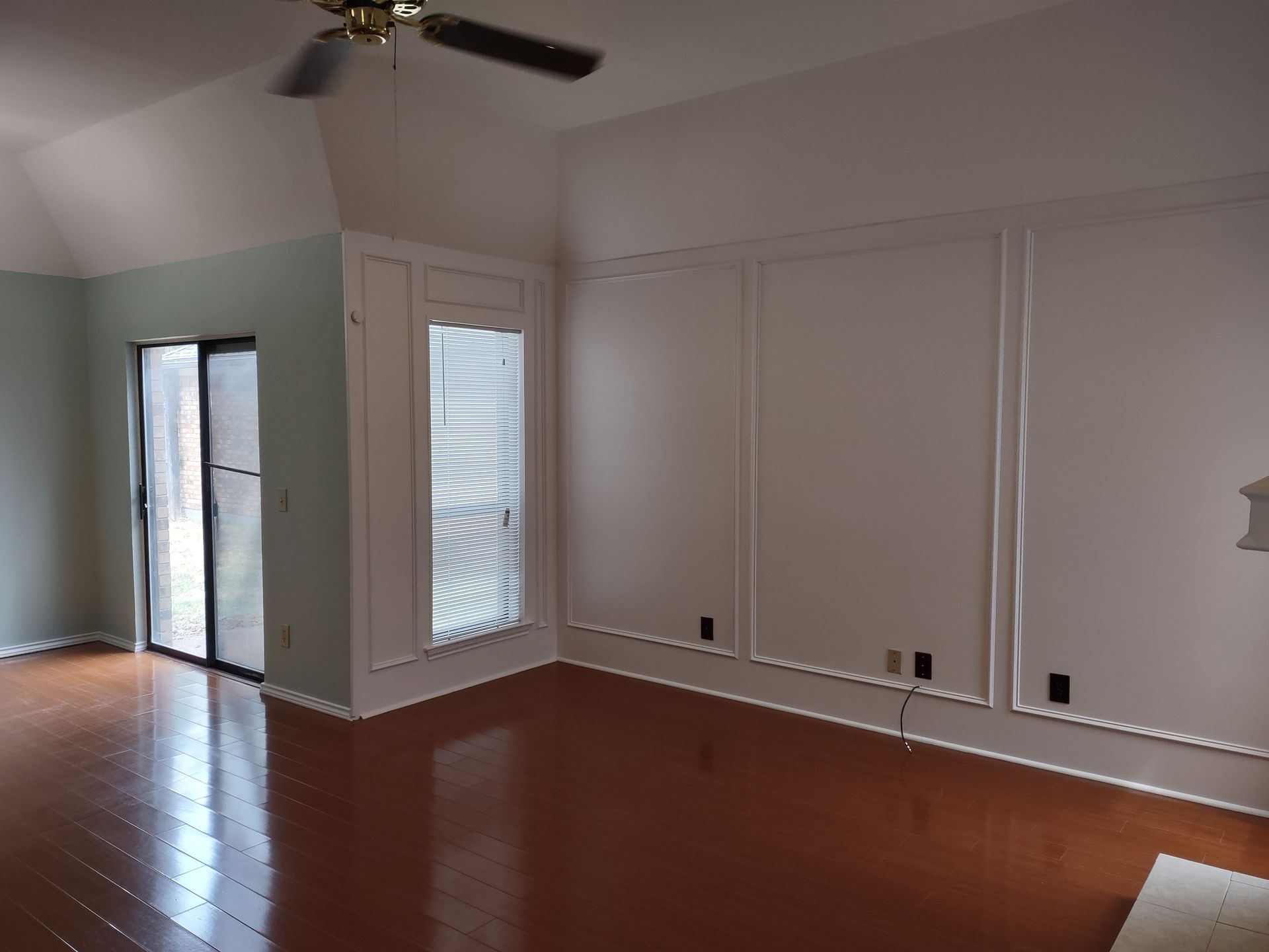 An empty living room with hardwood floors and a ceiling fan