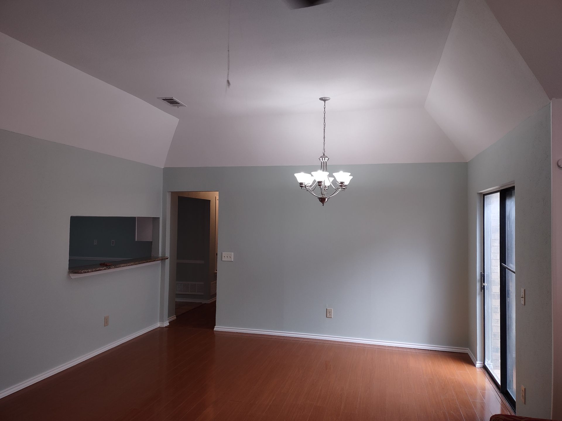 An empty living room with a chandelier hanging from the ceiling