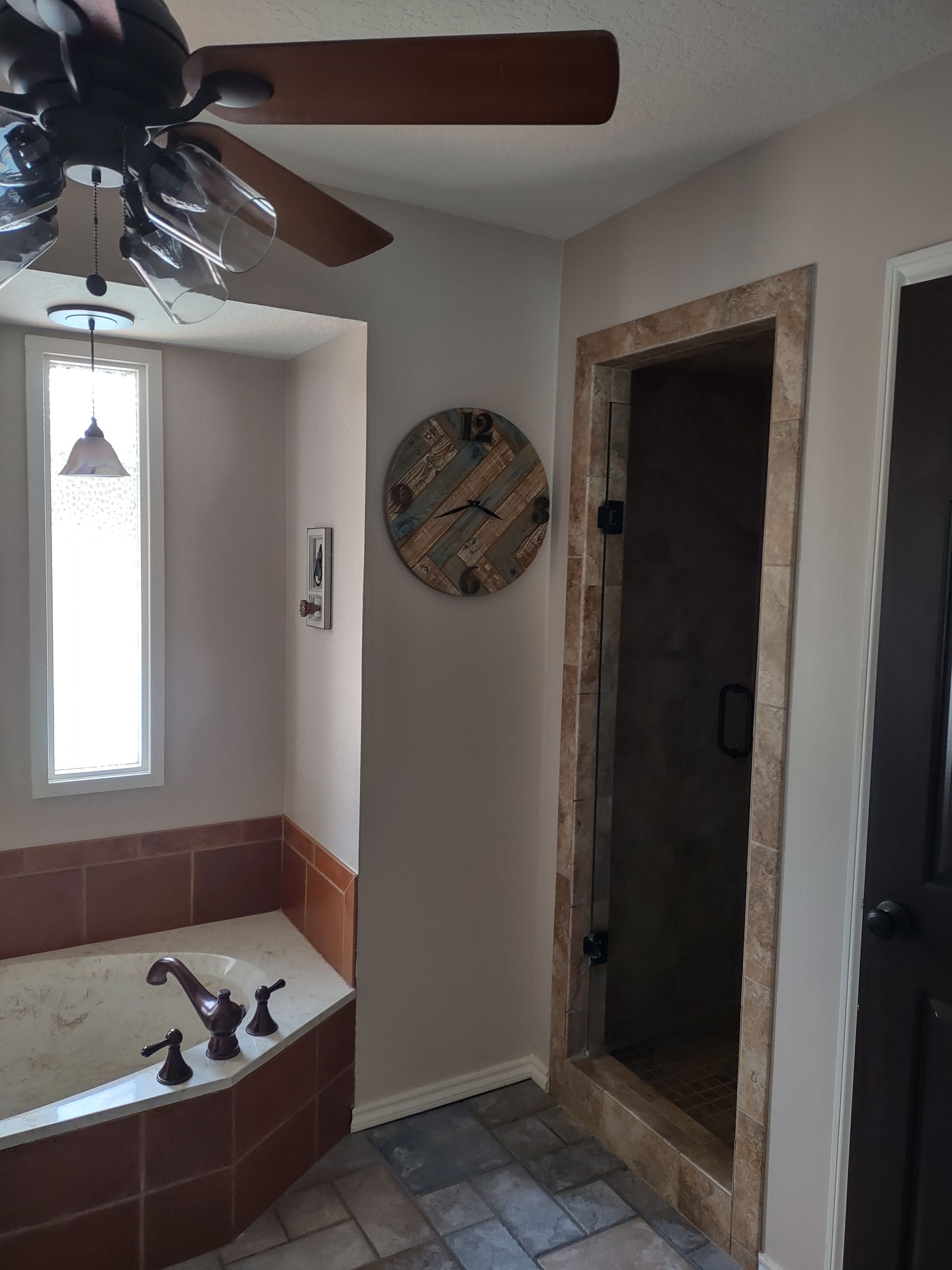 A bathroom with a tub , shower , ceiling fan and a clock on the wall.