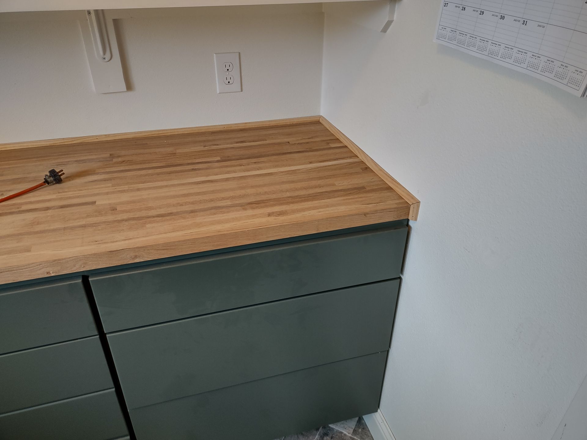 A kitchen counter with a wooden counter top and green cabinets.