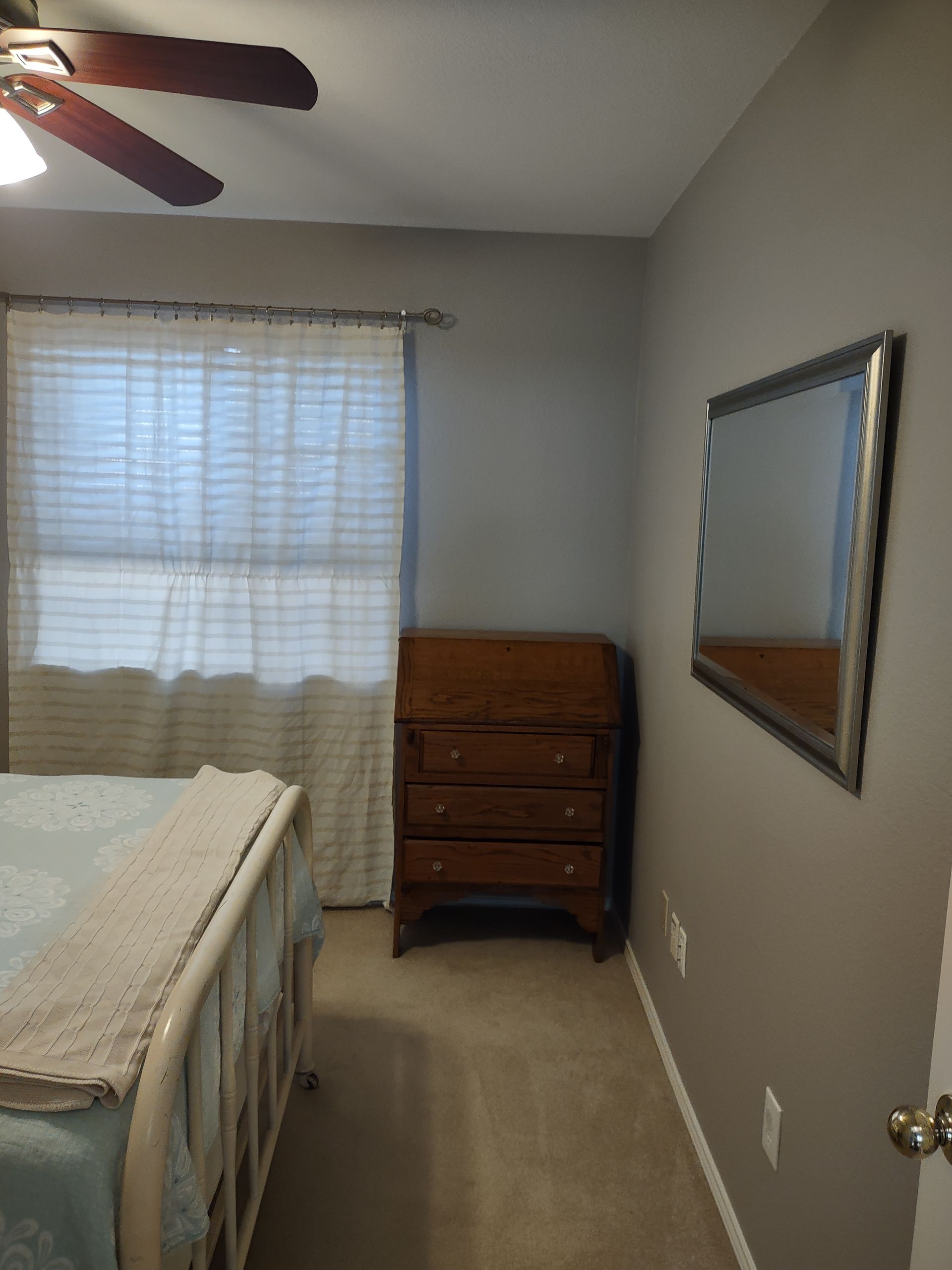 A bedroom with a bed , dresser , mirror and ceiling fan