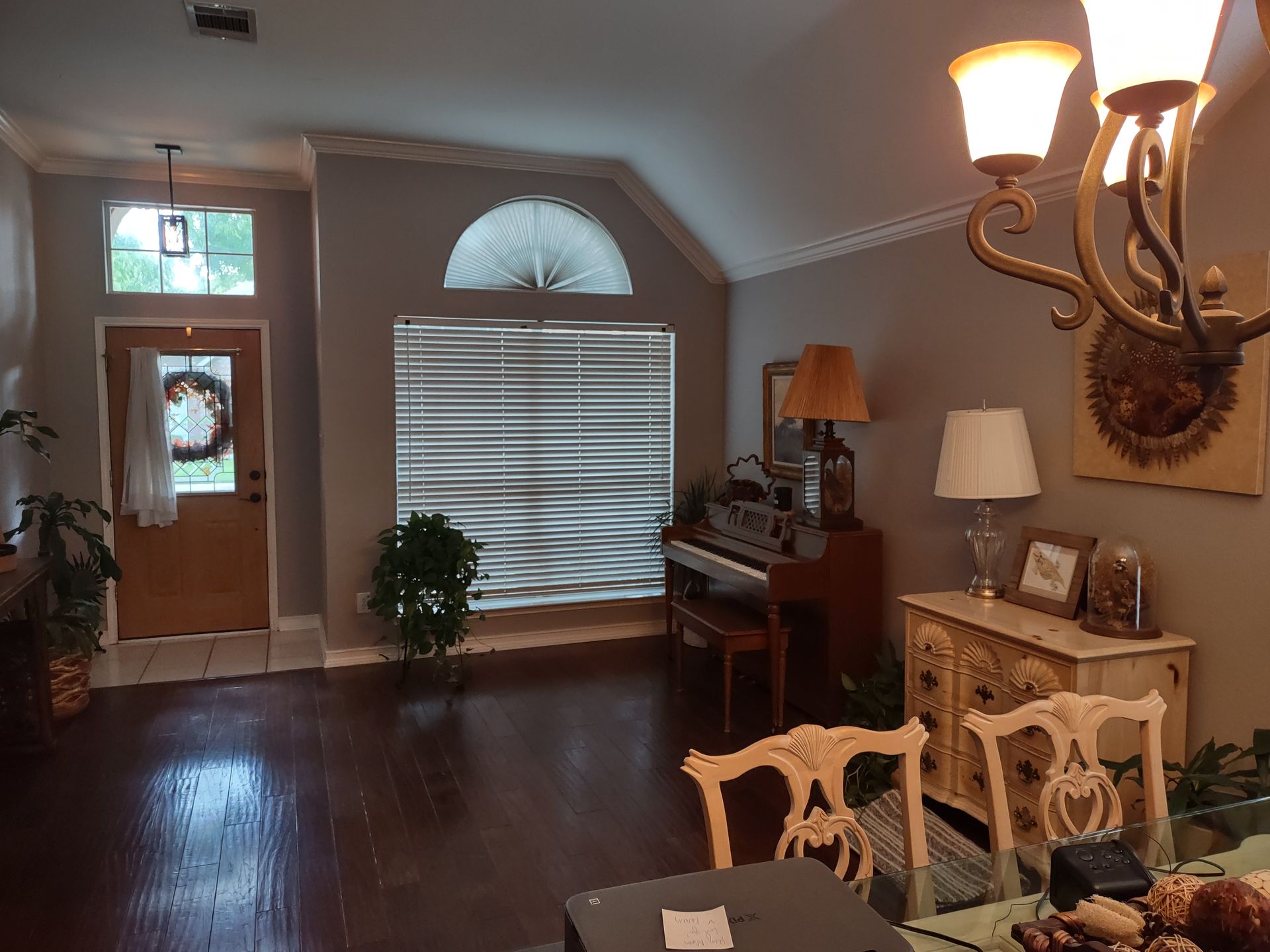 A living room with a piano , chairs , a table and a chandelier.