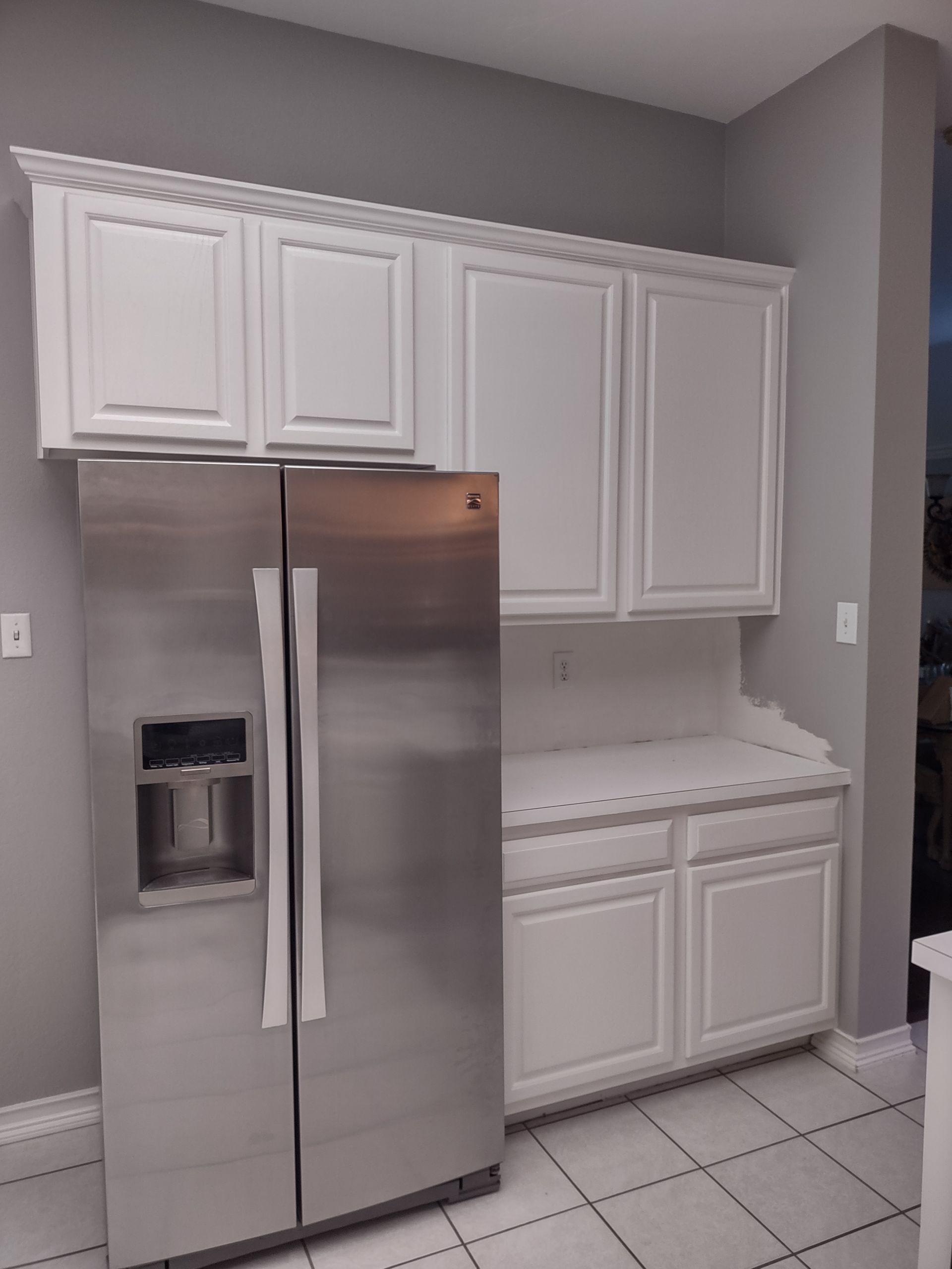 A kitchen with white cabinets and a stainless steel refrigerator