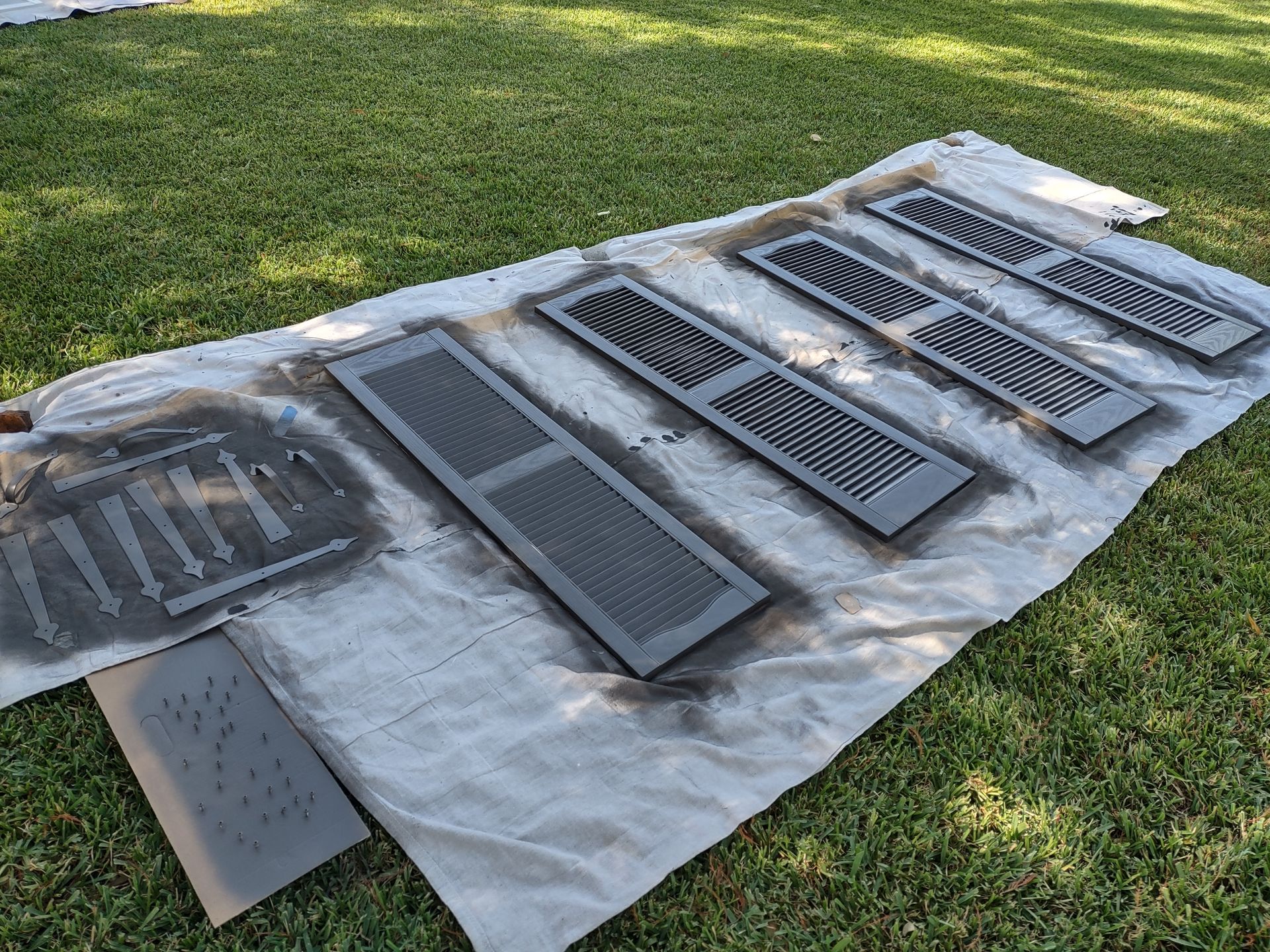 A bunch of shutters are sitting on top of a white cloth on the grass.