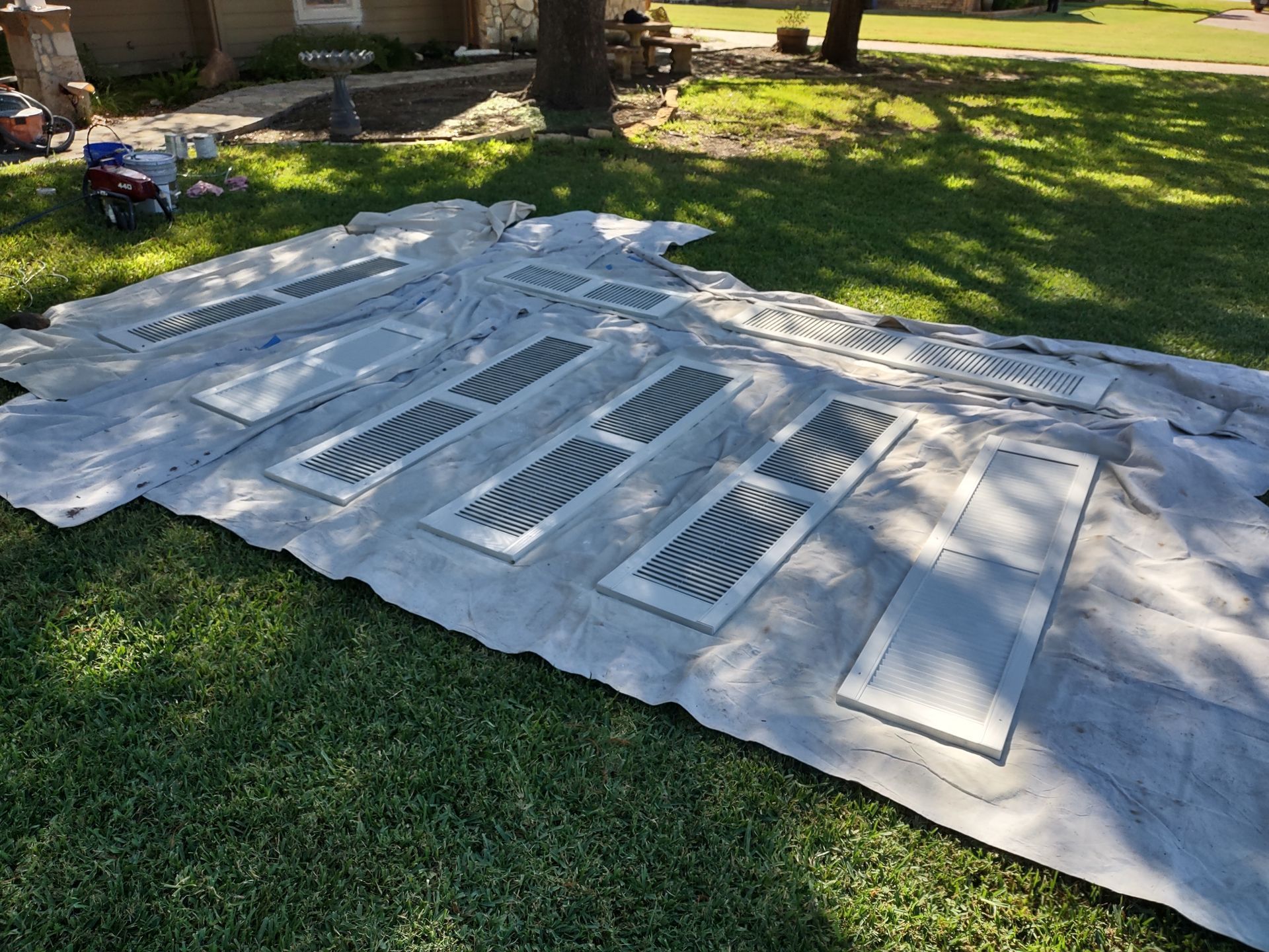 A bunch of shutters are sitting on top of a tarp on the grass.