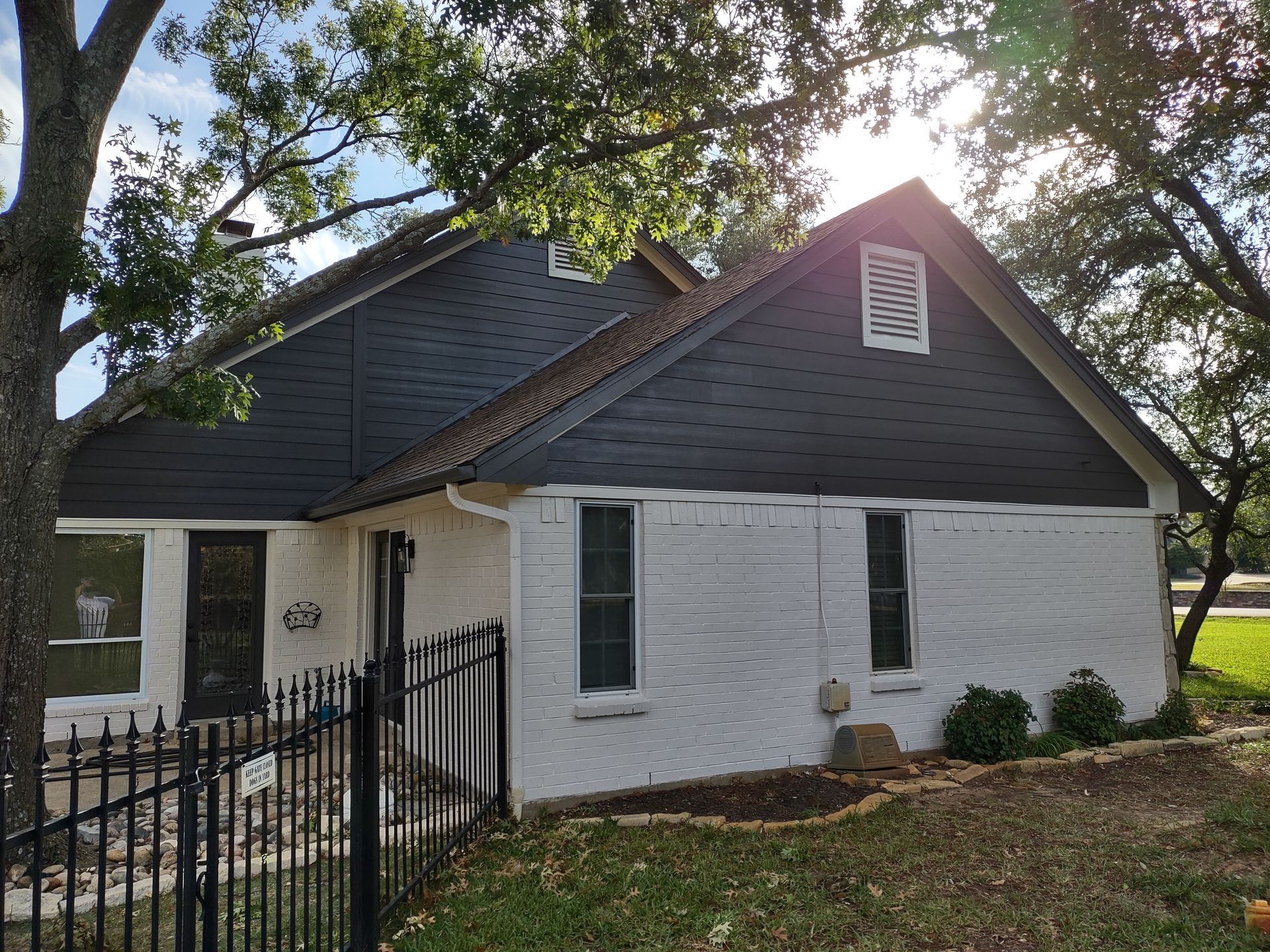 A white house with a black roof and a black fence in front of it.
