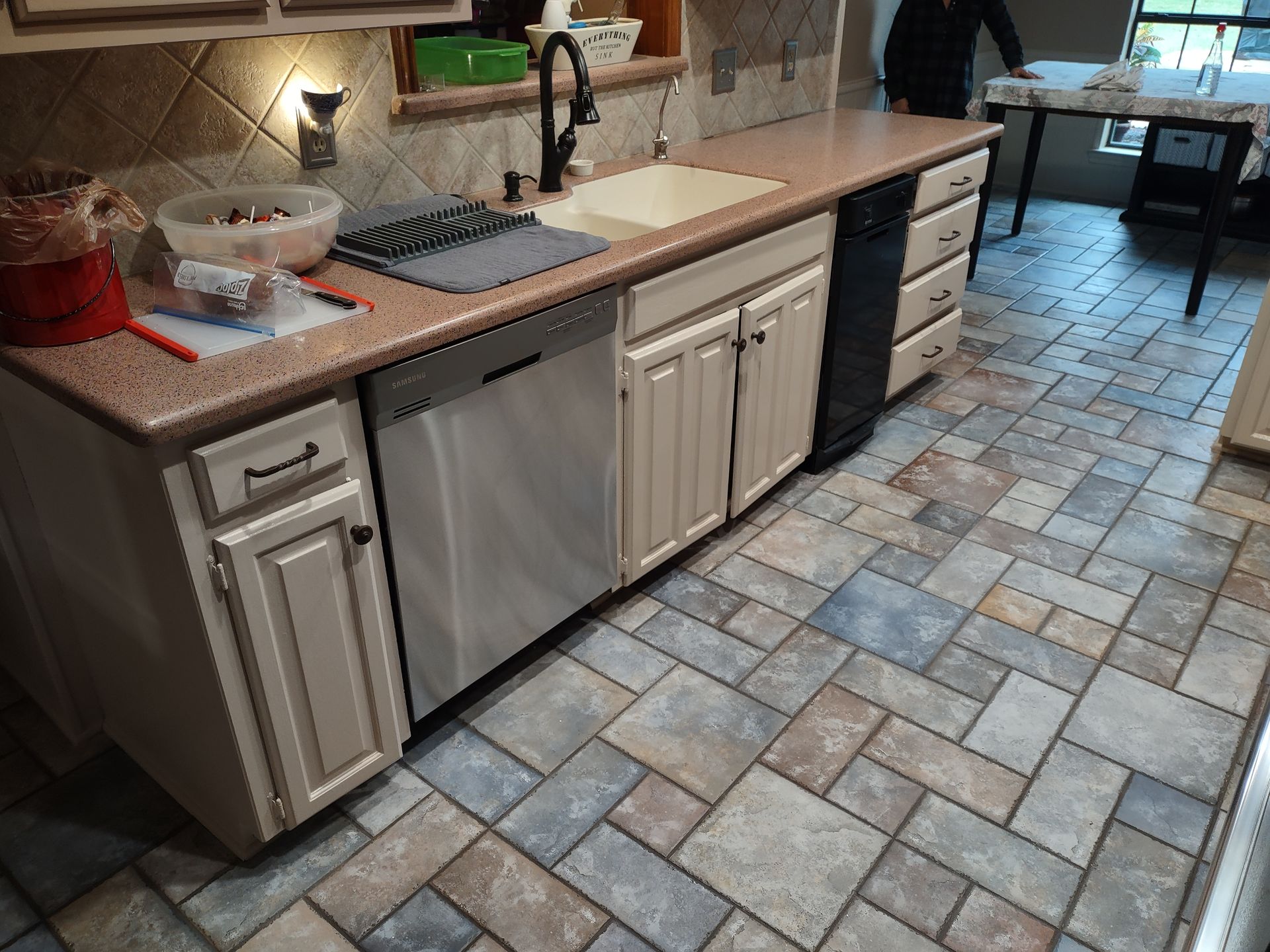 A kitchen with white cabinets , a sink , a dishwasher , and a tile floor.