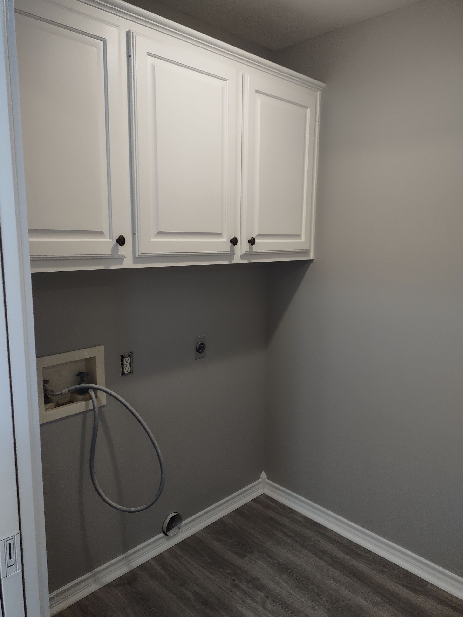 A laundry room with white cabinets and a hose attached to the wall.
