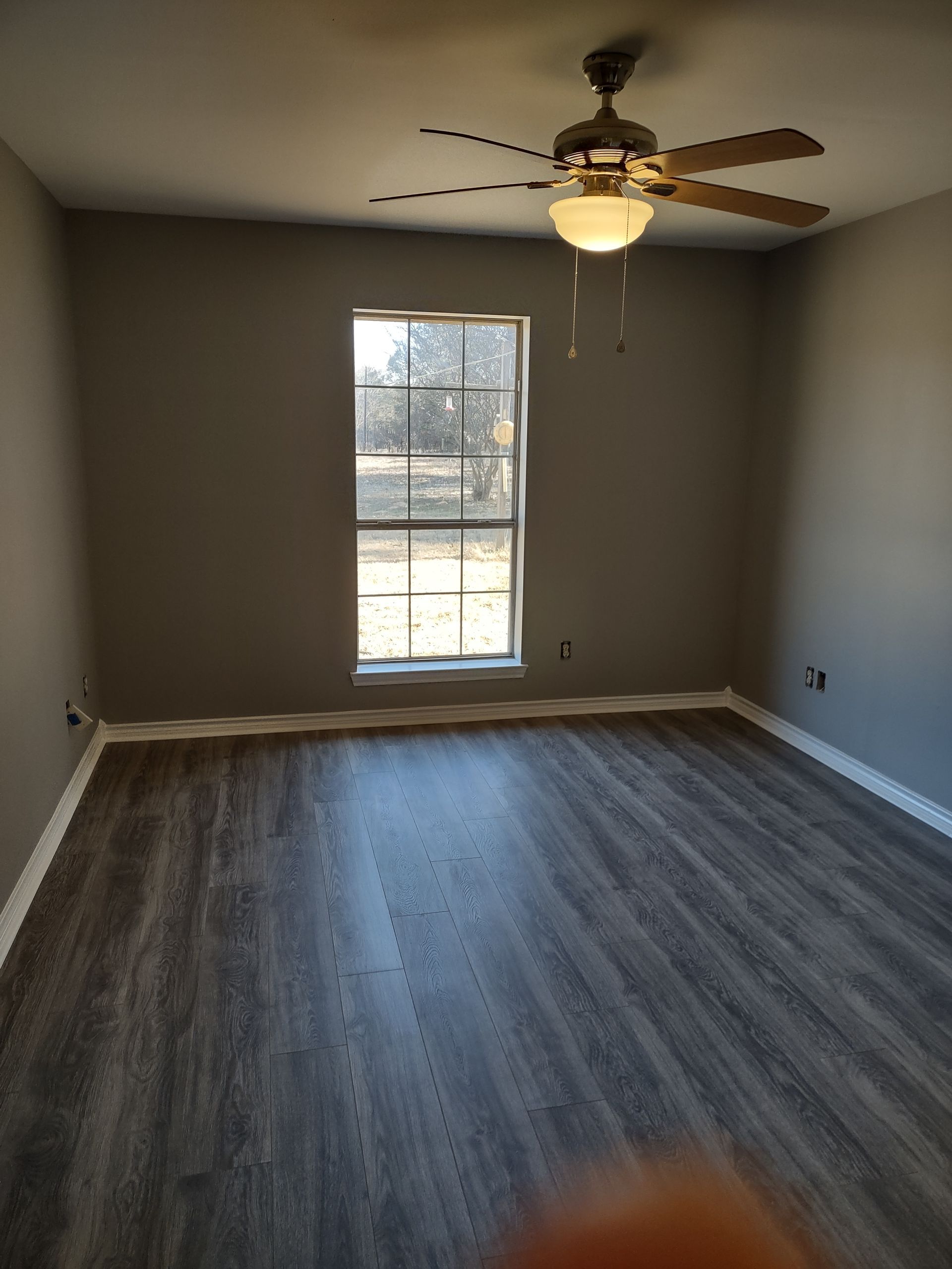 An empty room with a ceiling fan and a window.