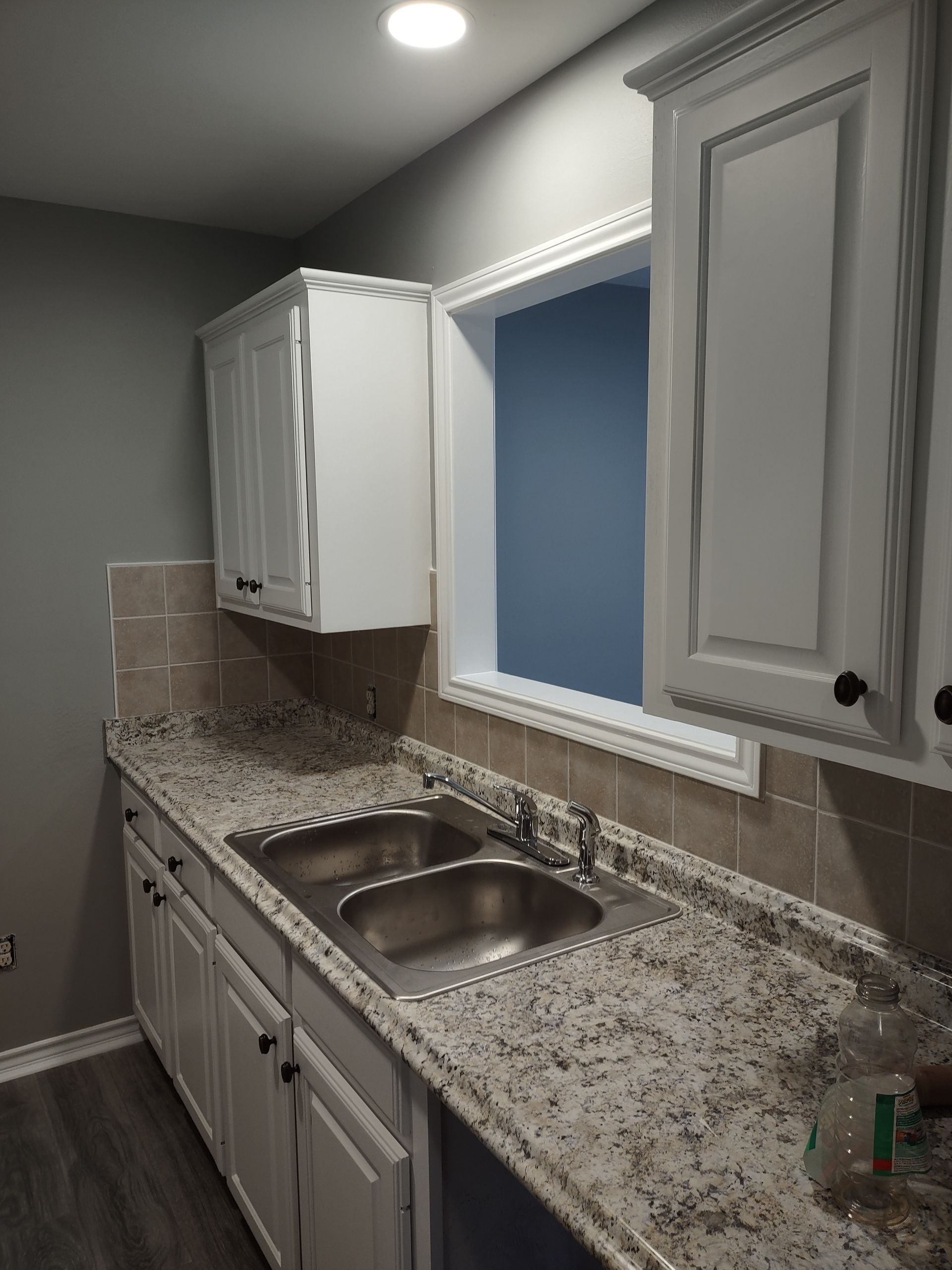 A kitchen with a sink , cabinets , granite counter tops and a window.