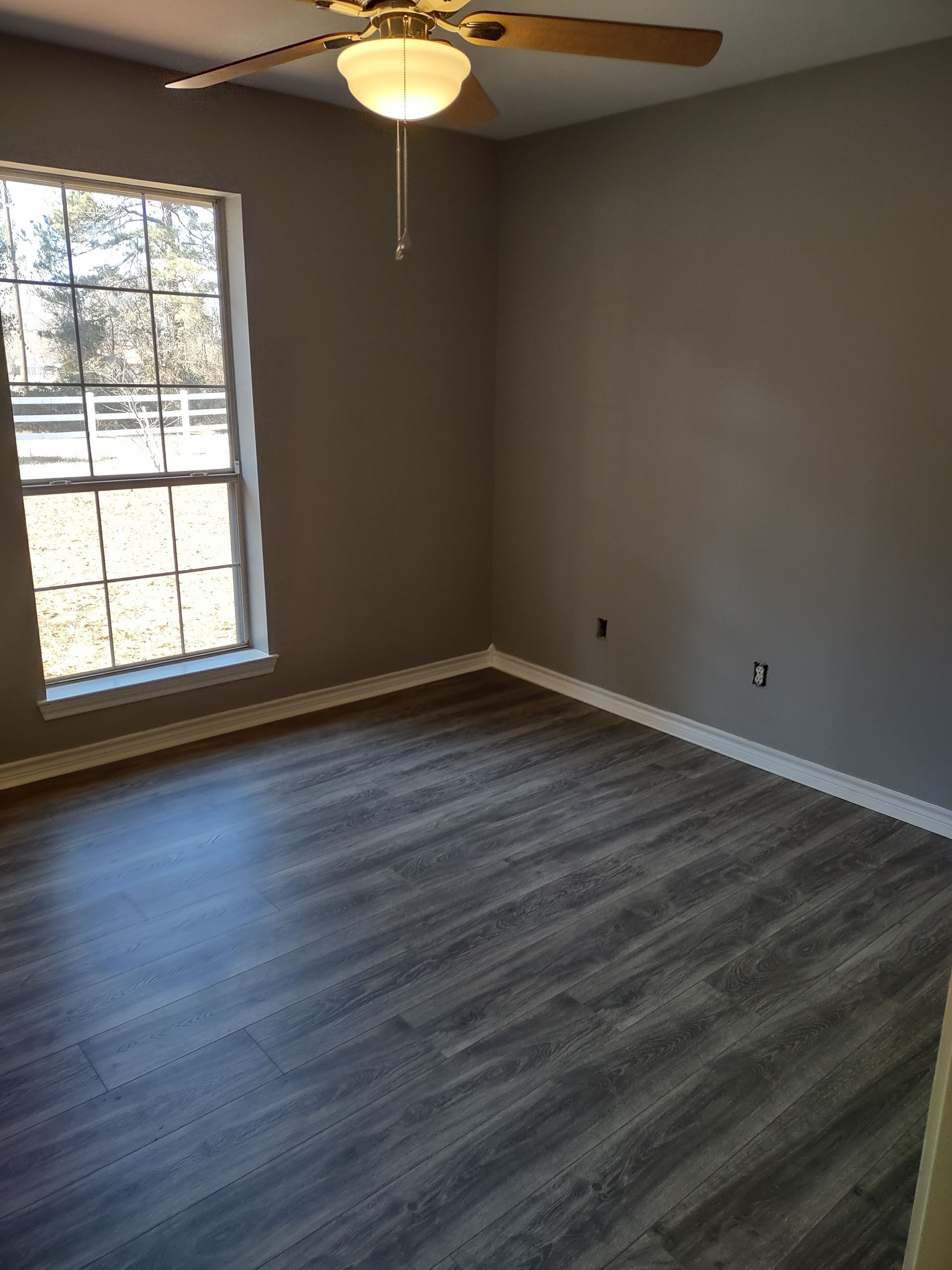 An empty room with a ceiling fan and a window.