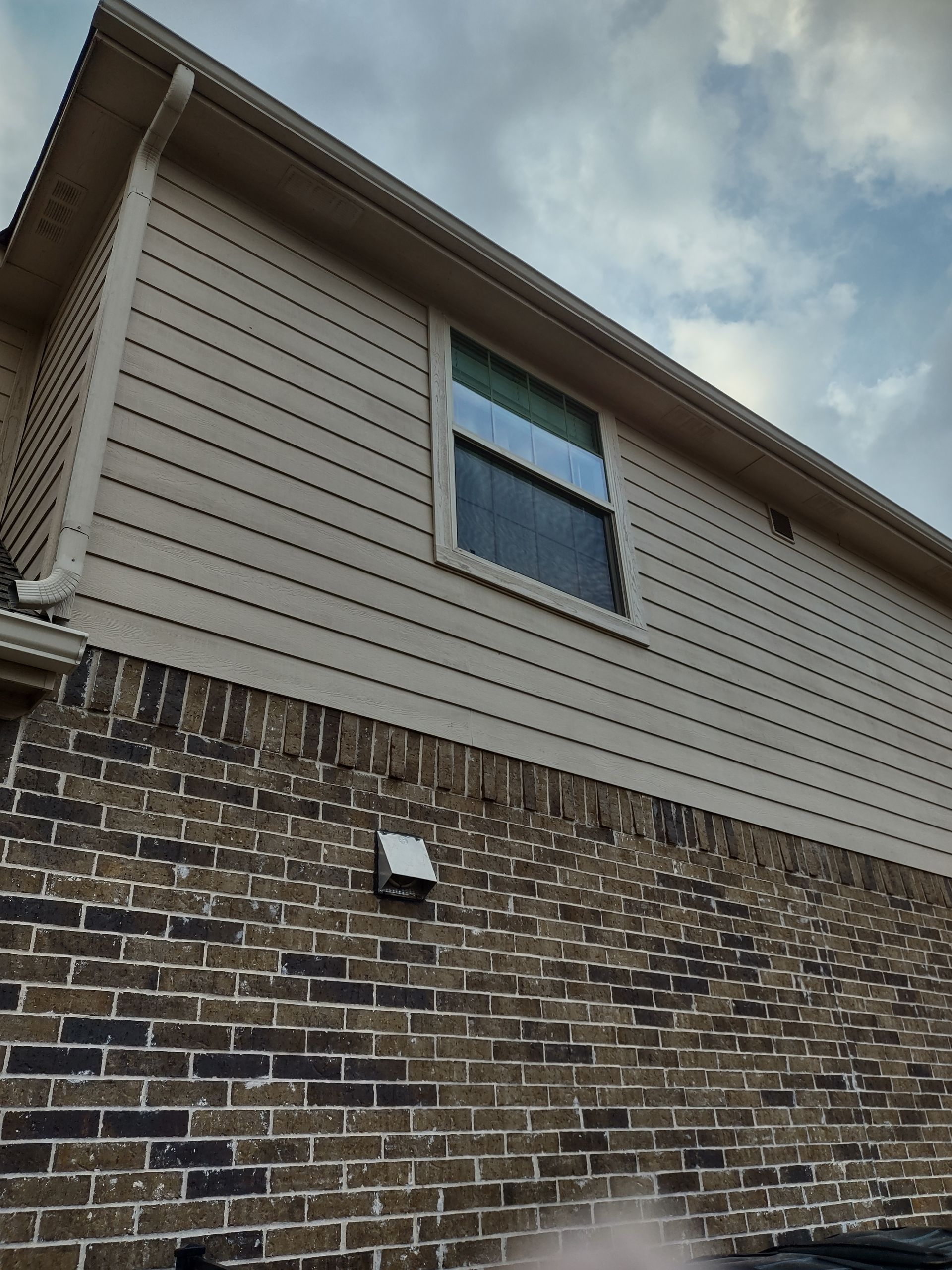 A brick building with a white siding and a window on the side.