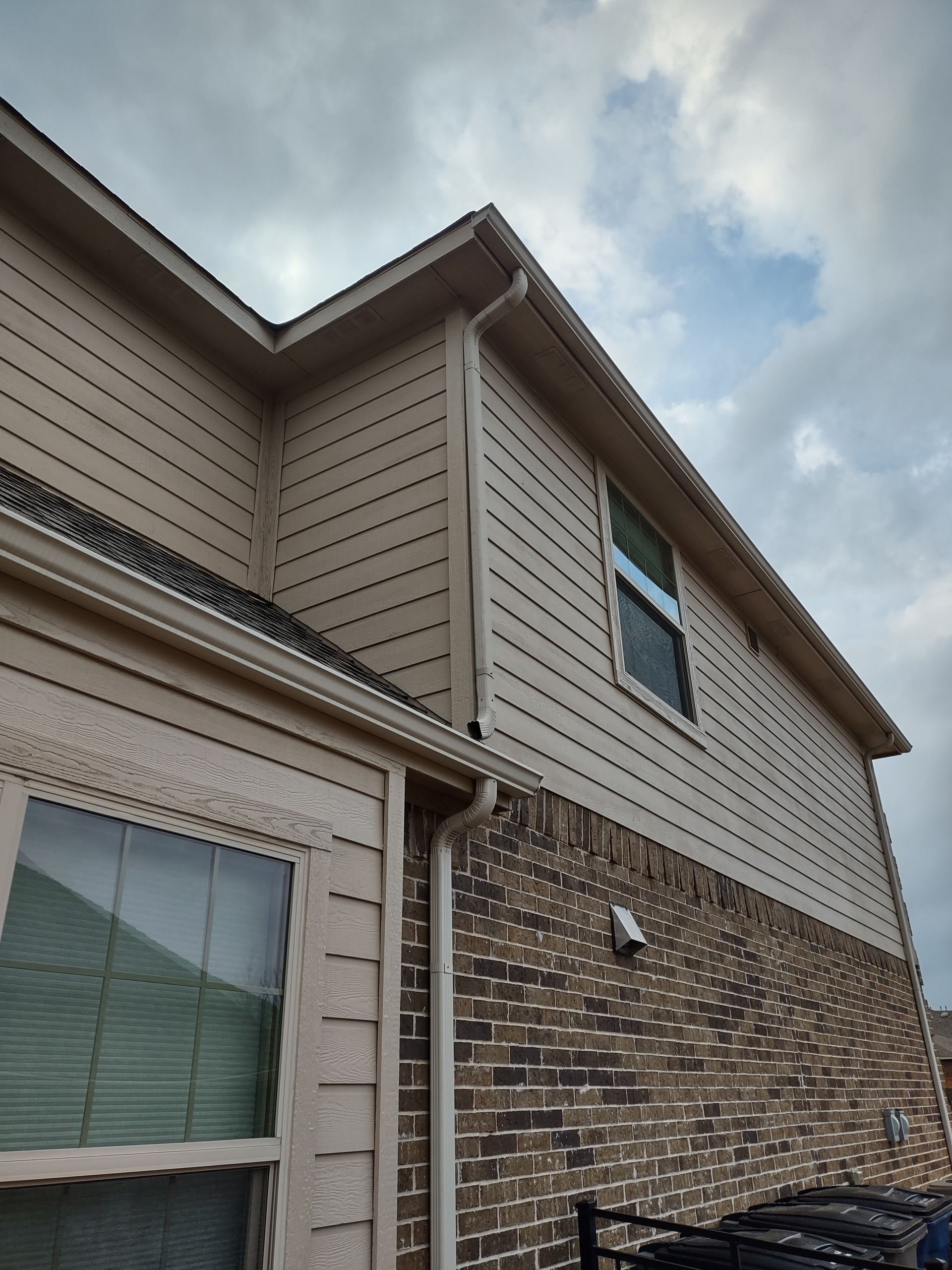 A large brick house with a tan siding and gutters.