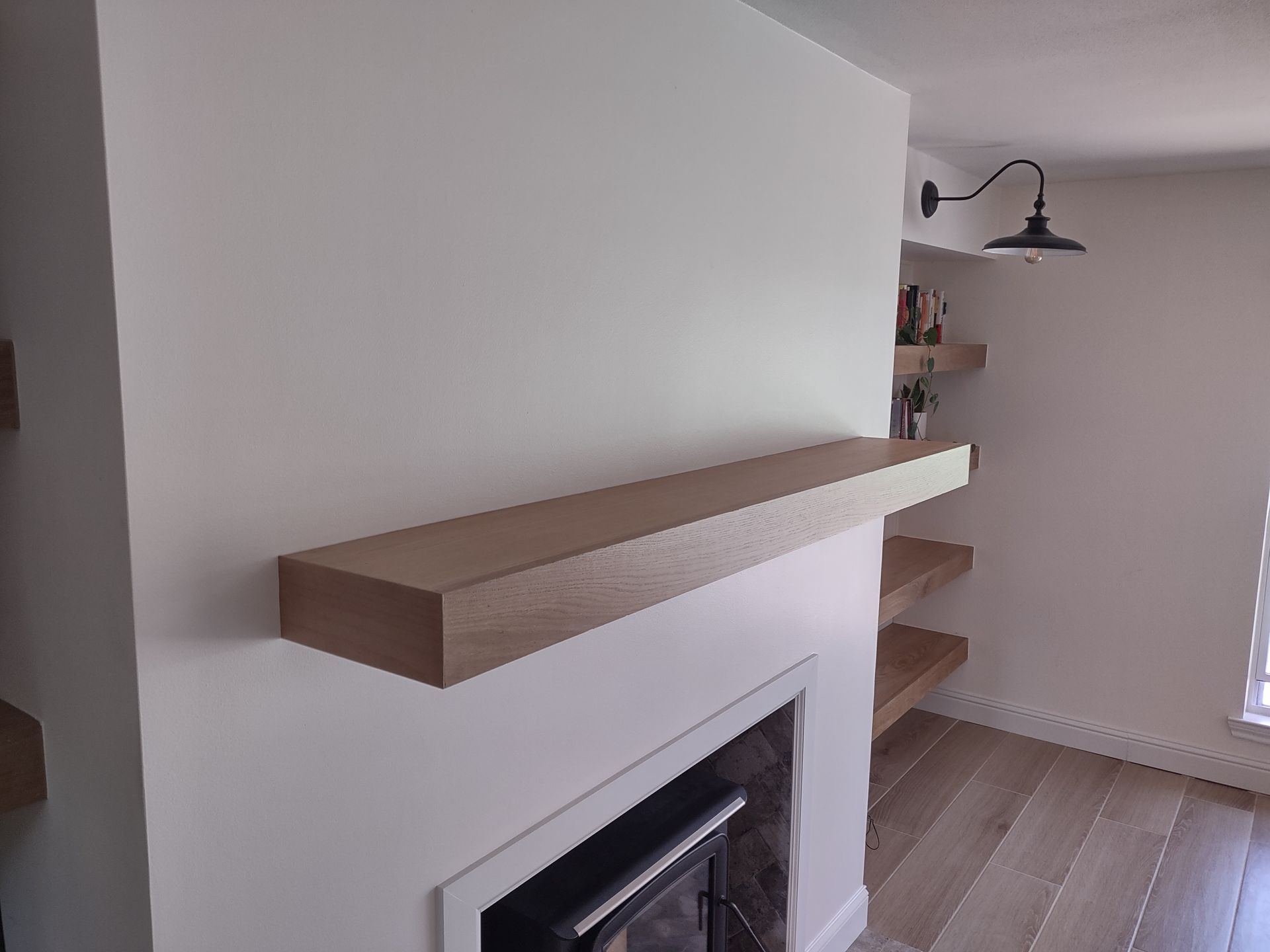 A living room with a fireplace and a wooden shelf above it.