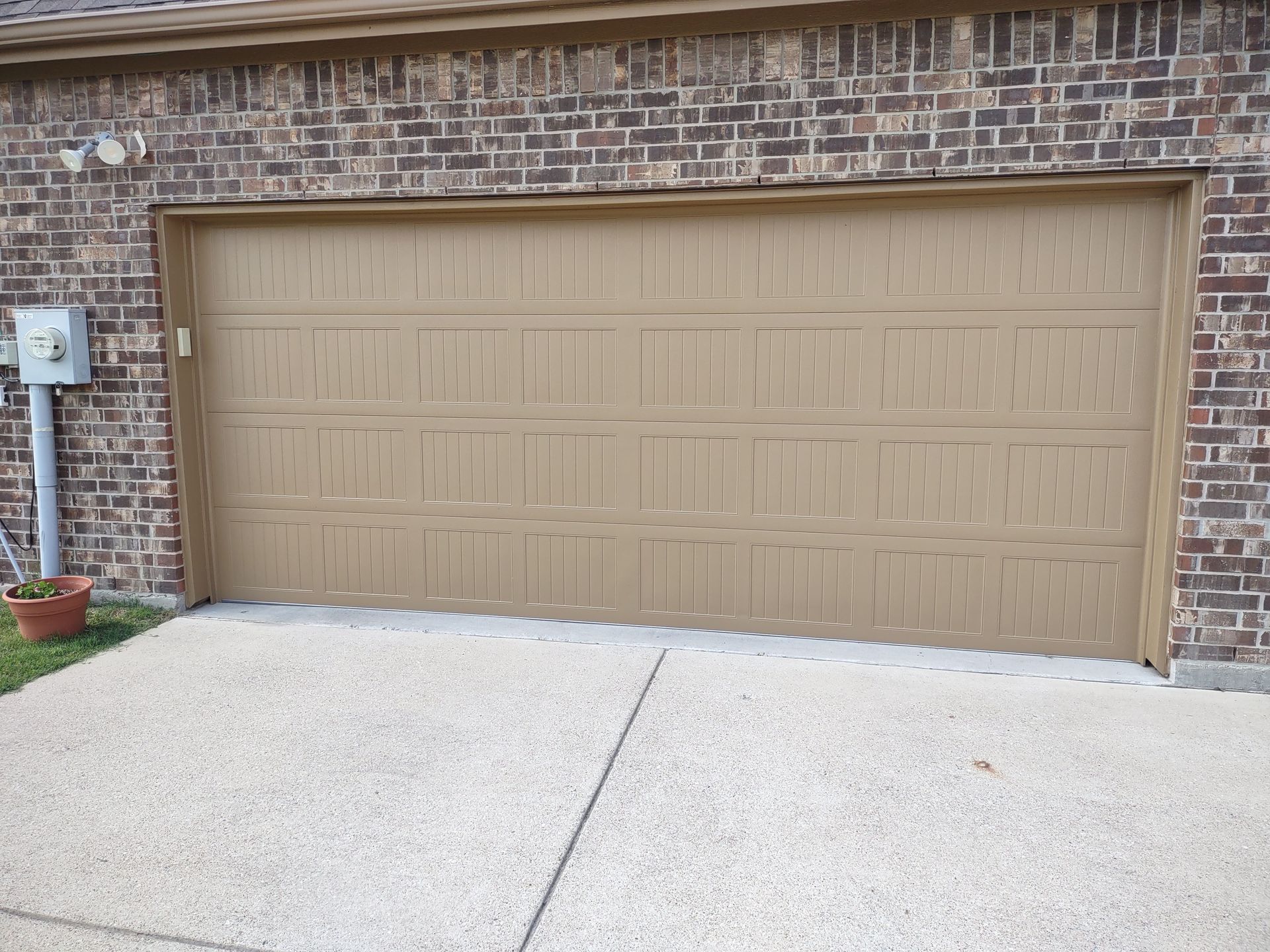 A brown garage door is sitting in front of a brick house.