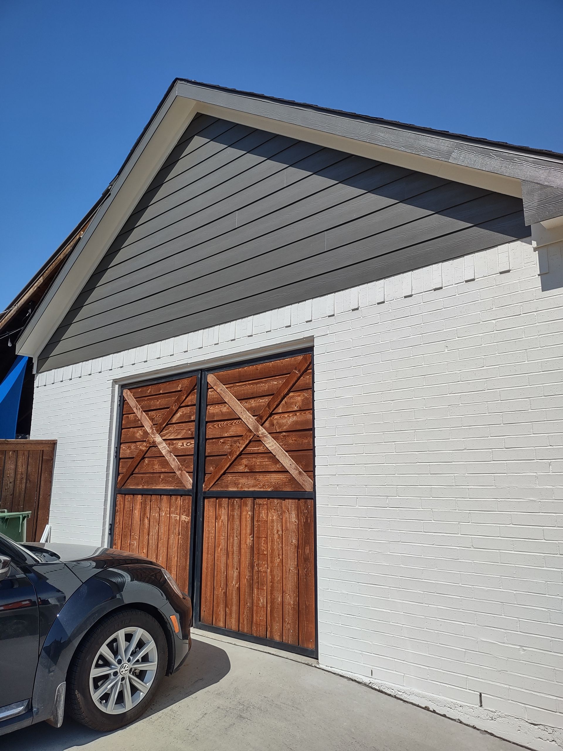 A car is parked in front of a garage with wooden doors.