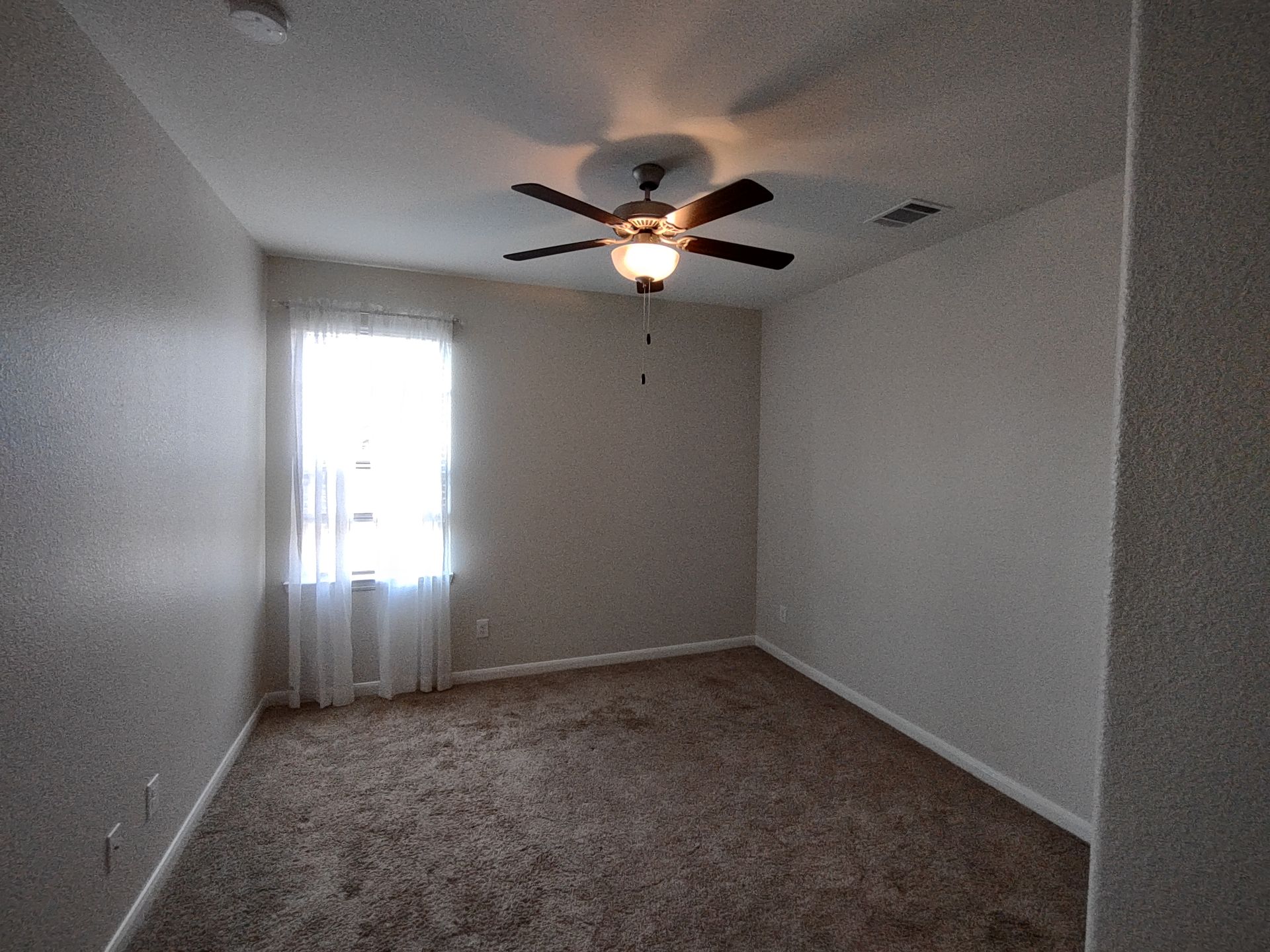 An empty bedroom with a ceiling fan and a window.