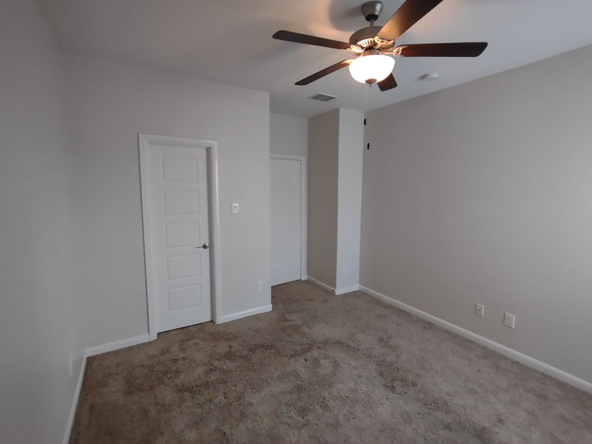 An empty bedroom with a ceiling fan and a door