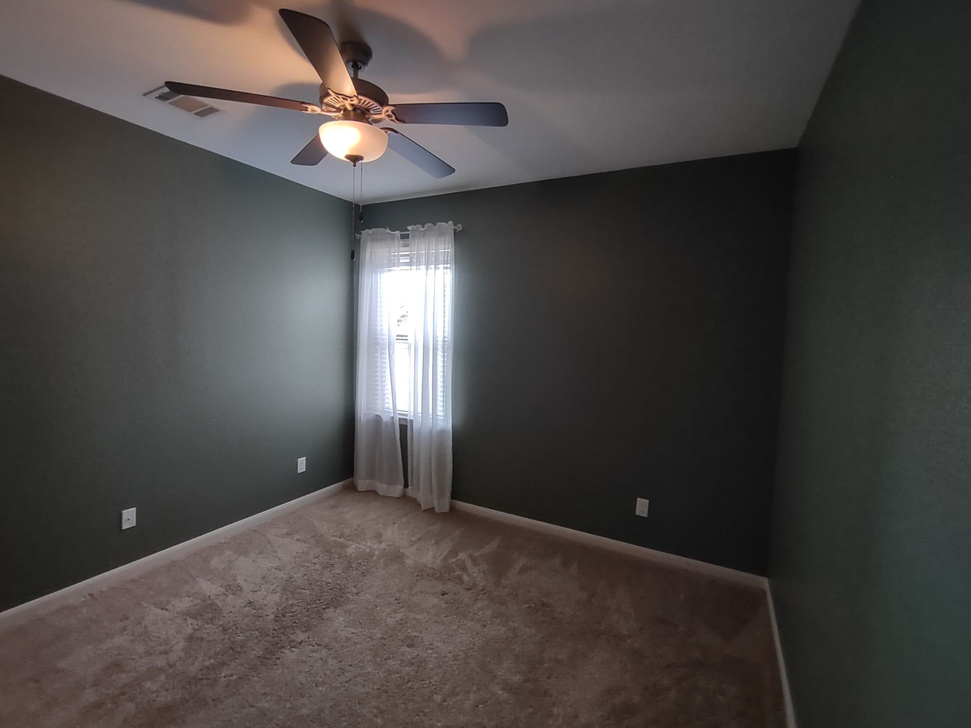 An empty bedroom with a ceiling fan and a window