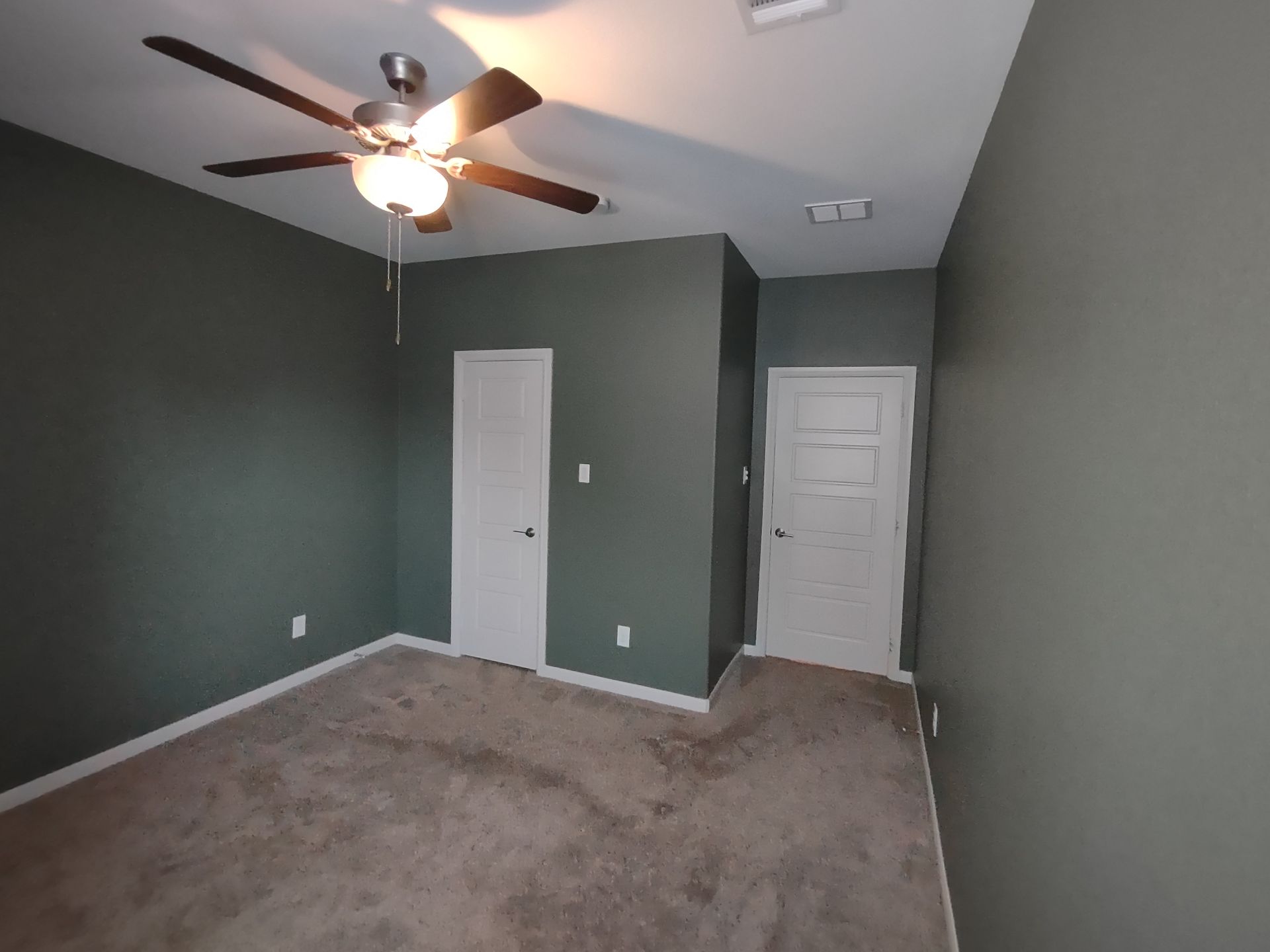 An empty bedroom with a ceiling fan and two doors