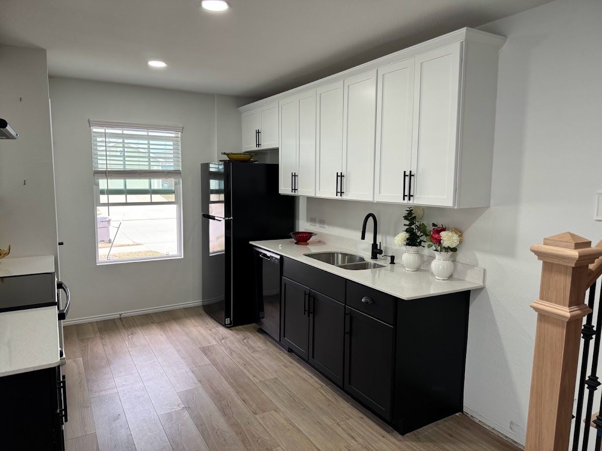 A kitchen with black cabinets , a black refrigerator , a sink , and a window.