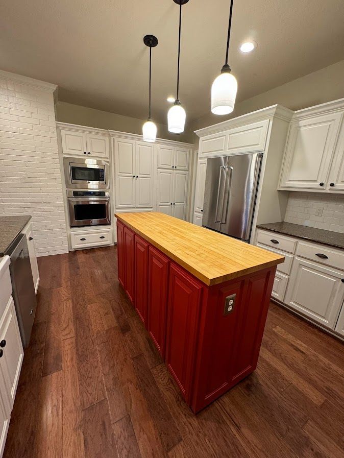 A kitchen with white cabinets and a large red island in the middle.