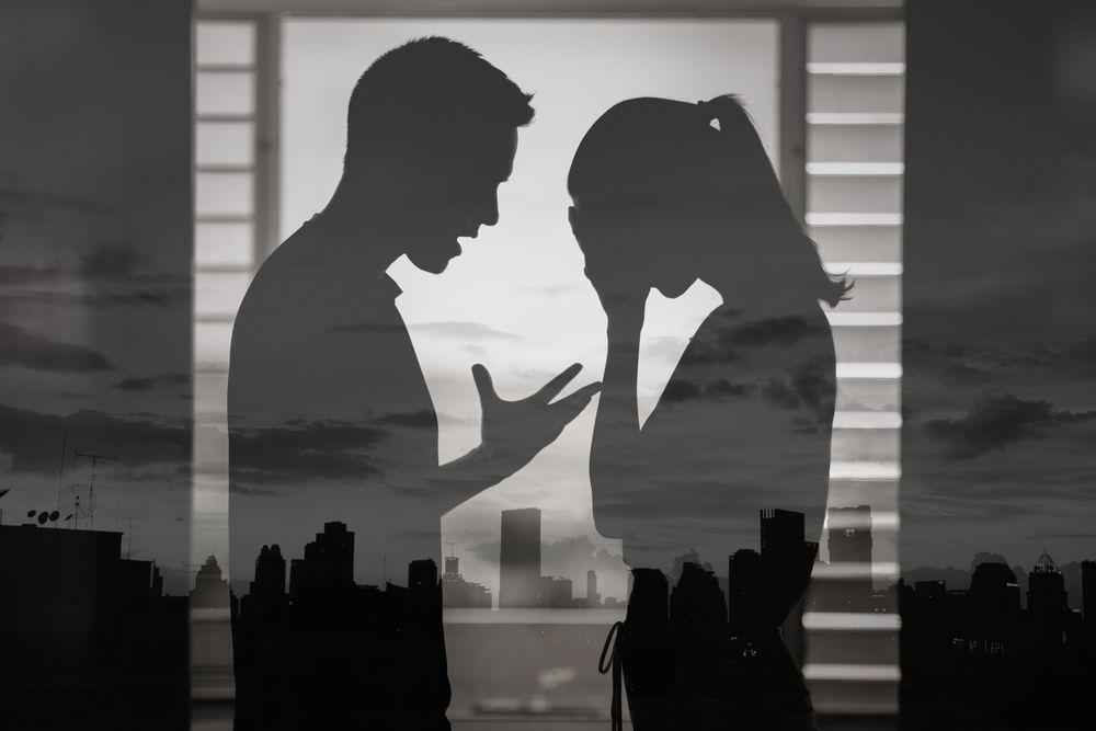 Black and white image of a couple in standing in front of a cityscape arguing -
