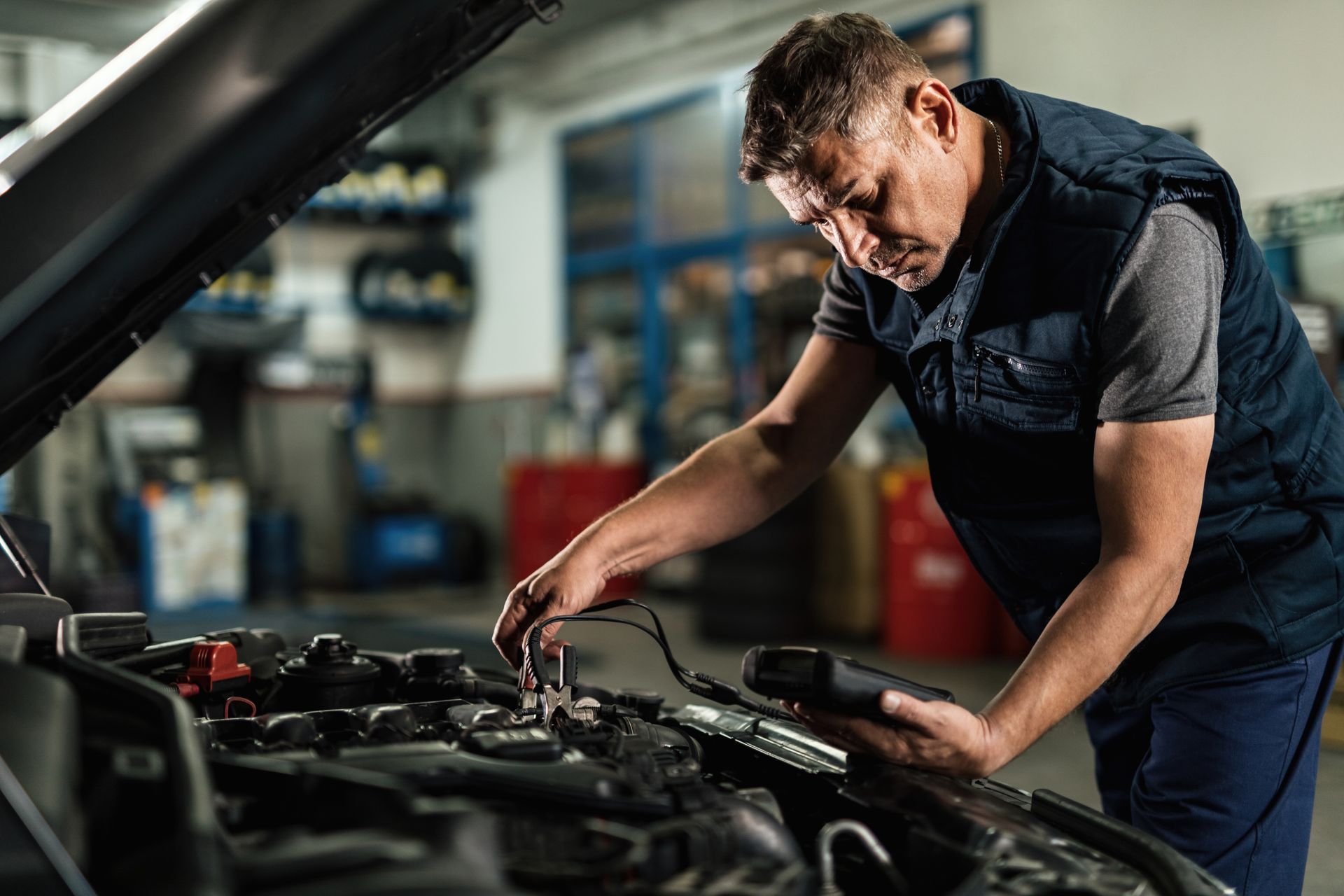 Mechanic working on a car engine in a garage; using a diagnostic tool.